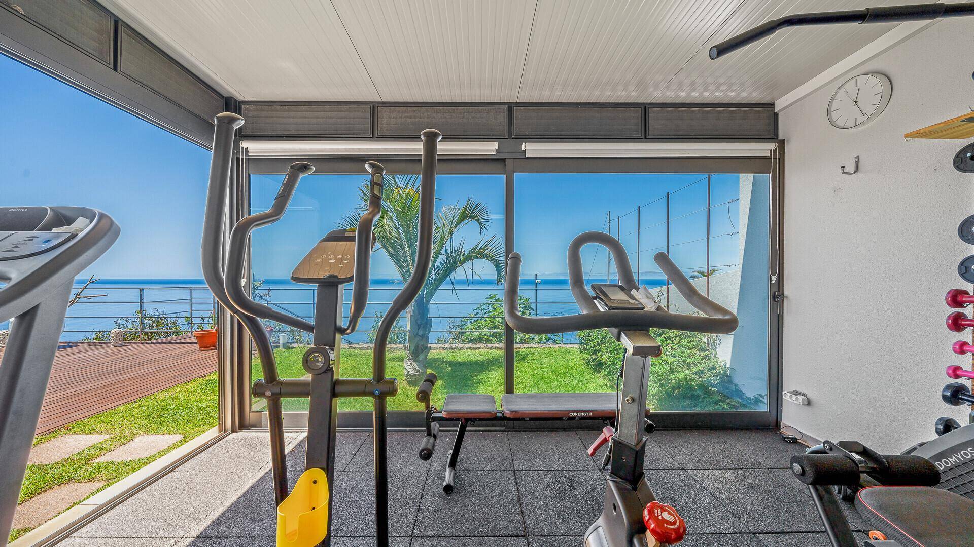 Heller Fitnessraum mit Meerblick, großen Fenstern und verschiedenen modernen Trainingsgeräten.