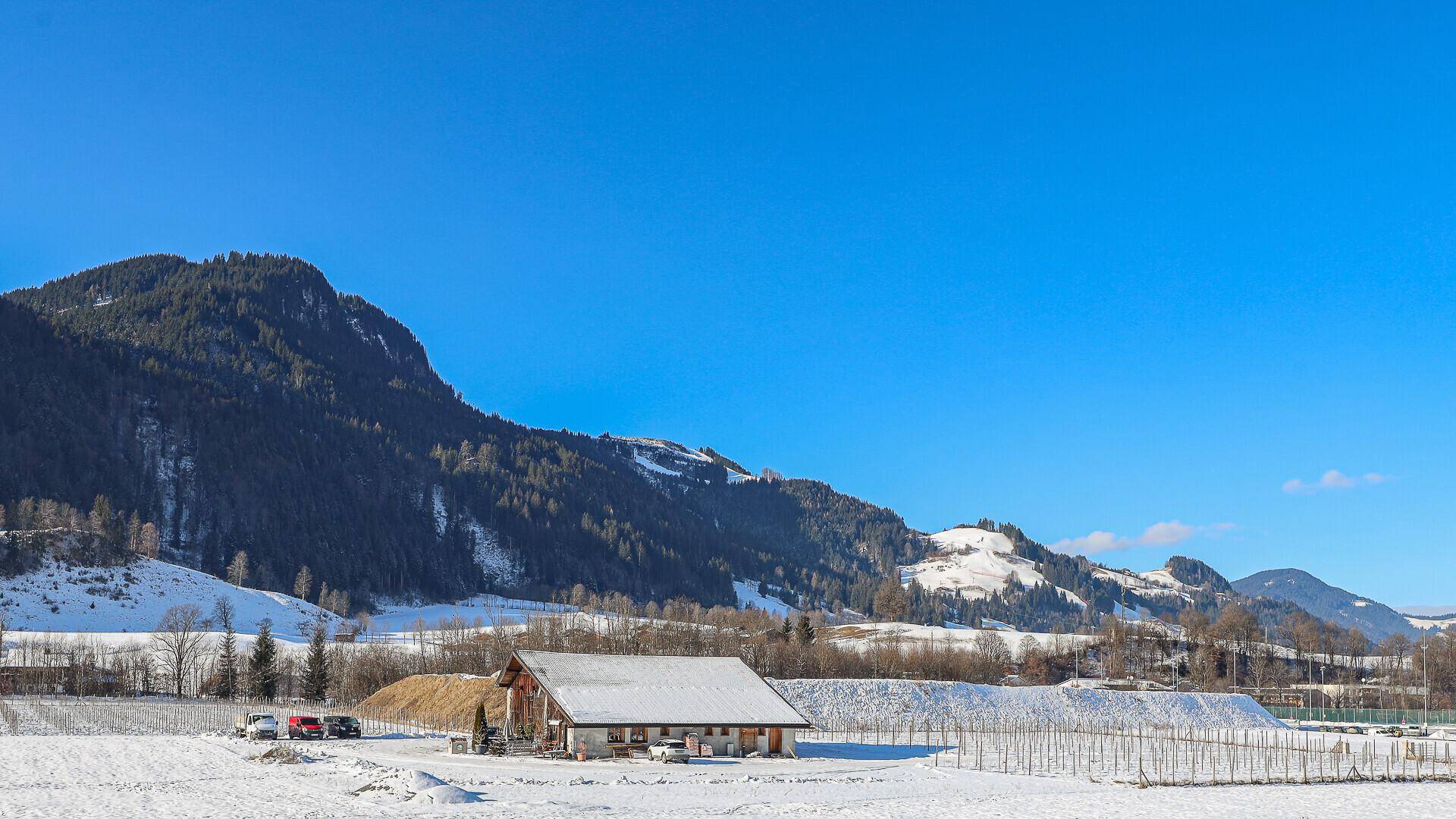 Malerische Winterlandschaft mit verschneiten Bergen und einem traditionellen Gebäude im Tal.