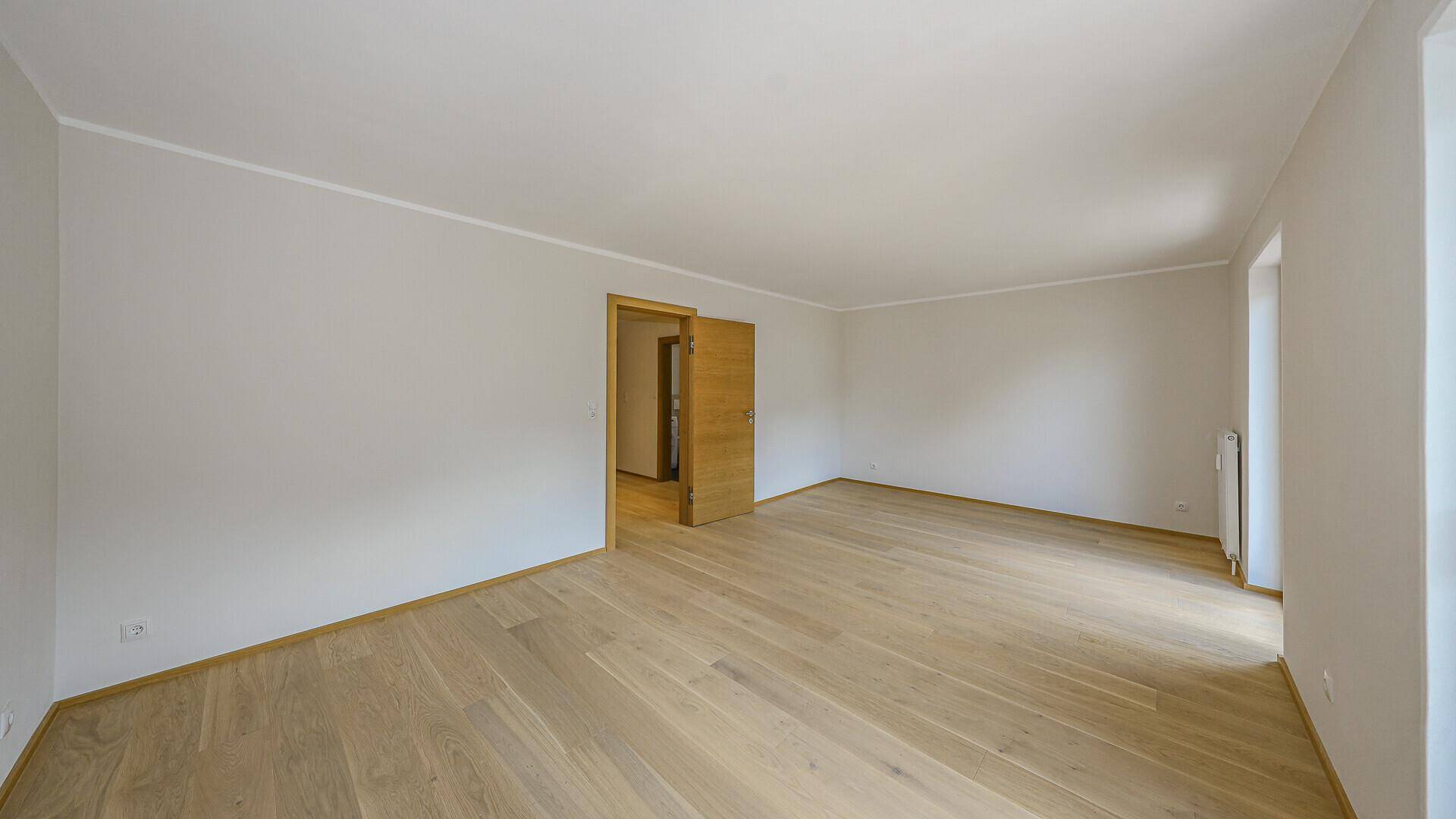 Leerer Raum mit hellem Holzboden und einer modernen Schiebetür, bietet vielseitige Nutzungsmöglichkeiten.