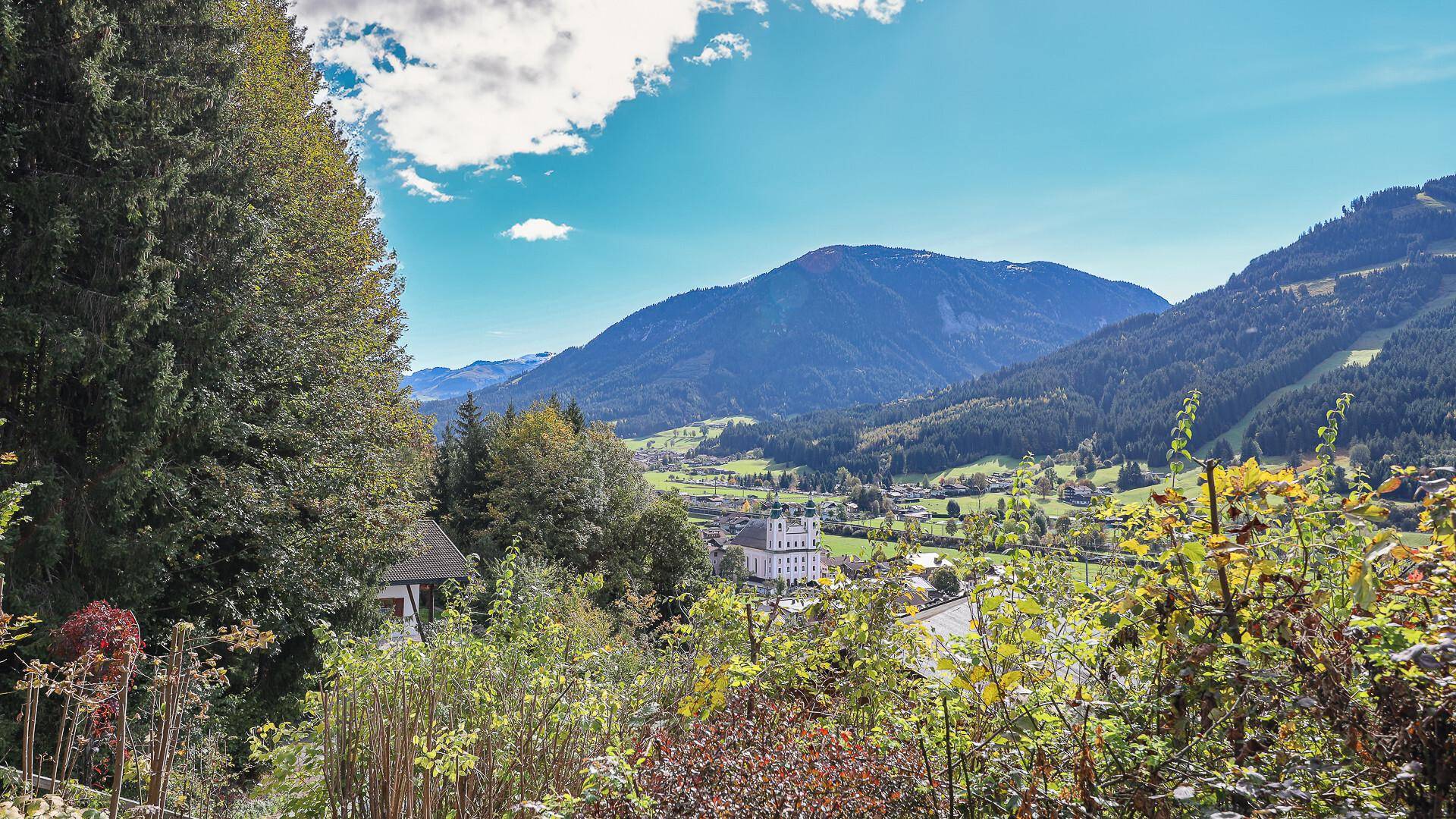 Idyllischer Ausblick auf ein charmantes Dorf und die umliegende Berglandschaft mit Wäldern.
