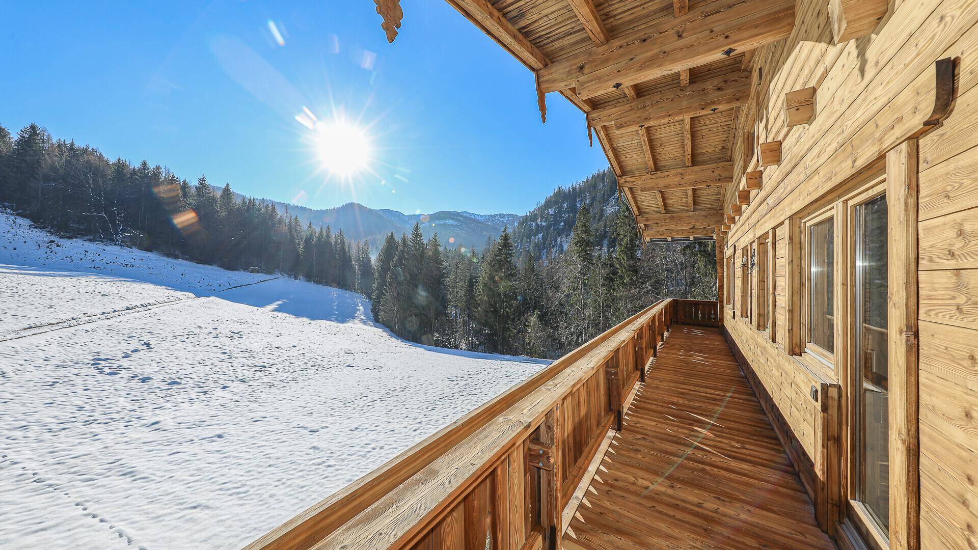 Geräumiger Holzbalkon mit sonnigem Ausblick auf die umliegenden Berge.