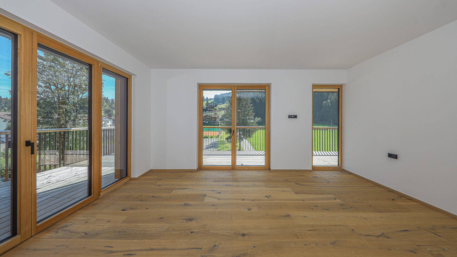 Geräumiger, heller Wohnbereich mit Holzboden und mehreren Fenstern mit Bergblick.