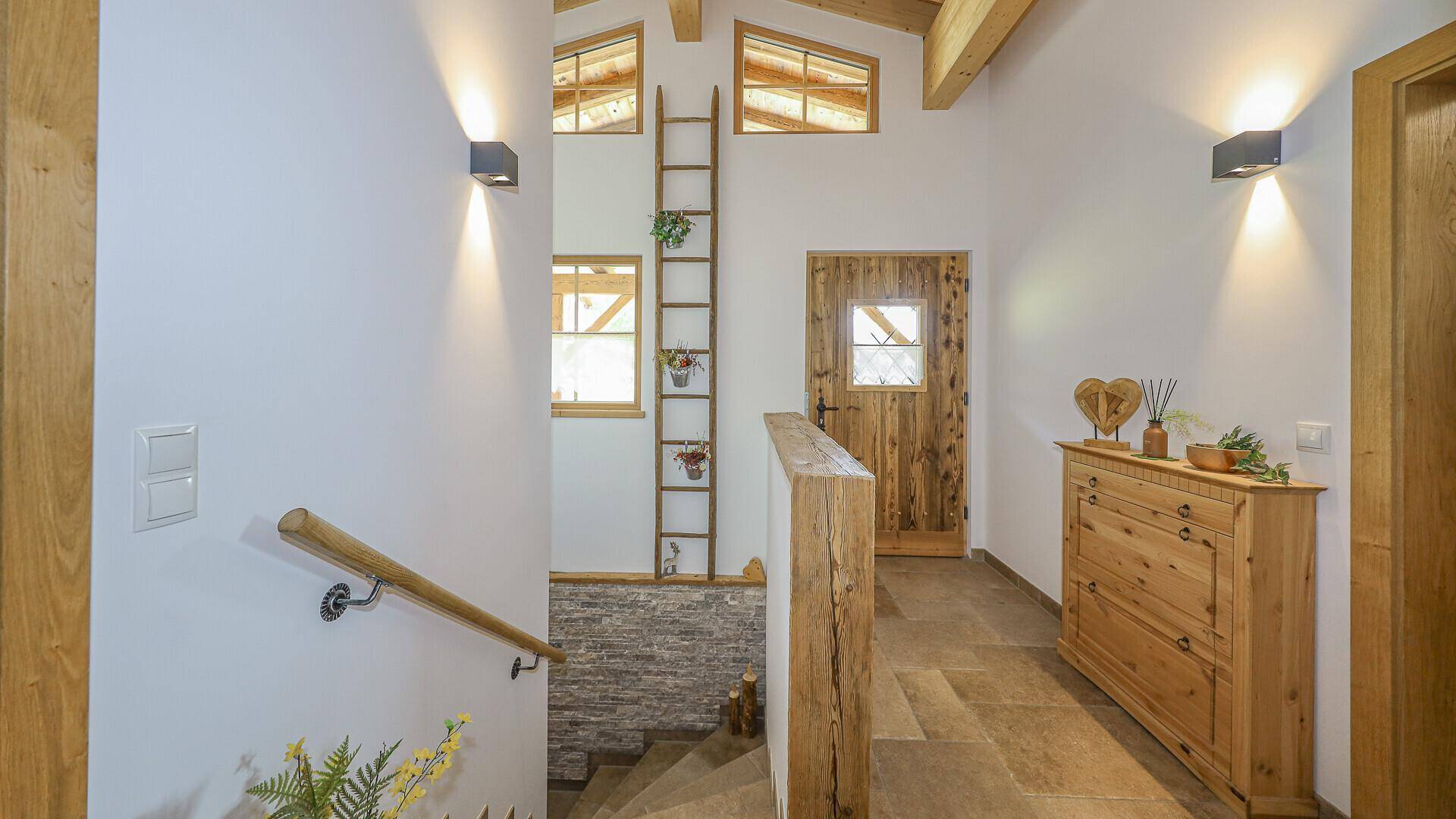 Heller Flur mit Holztreppe, Steinfliesenboden und rustikaler Holzkommode.