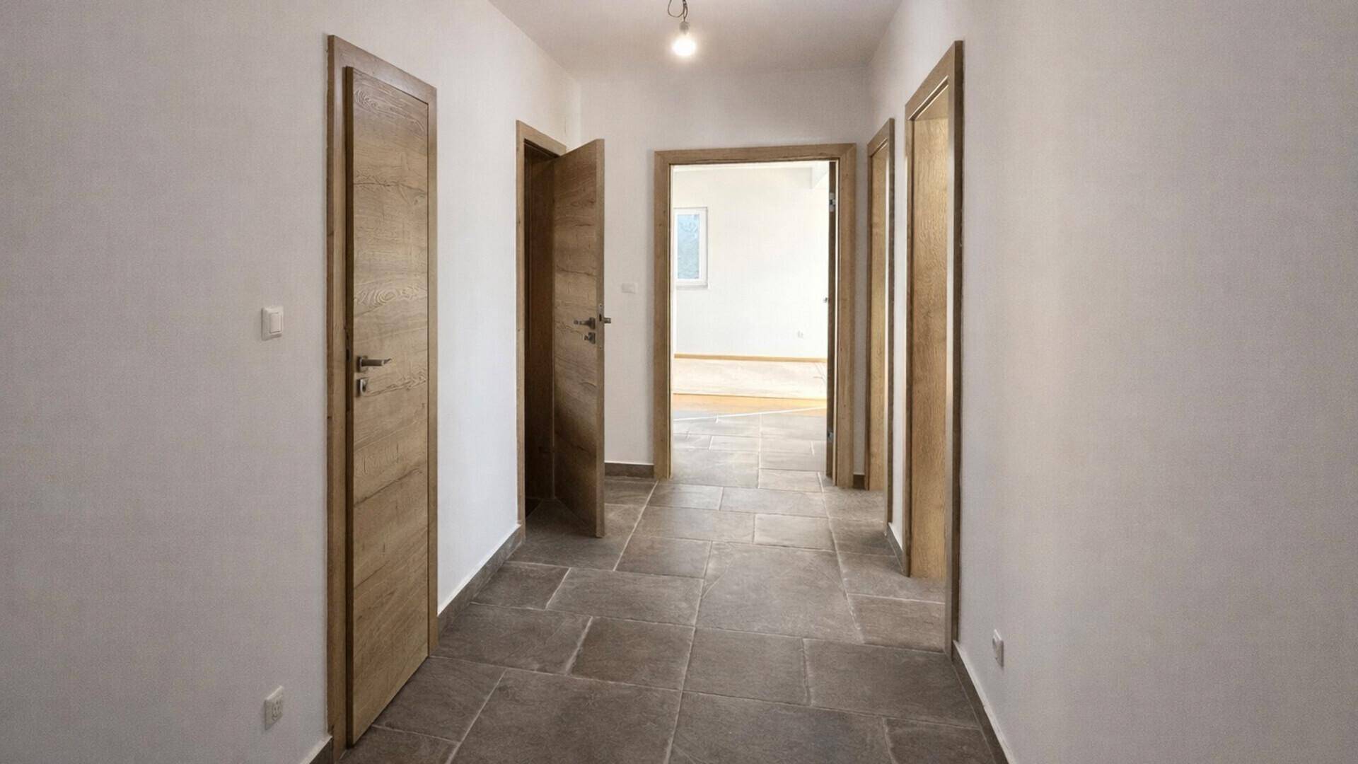 Geräumiger Flur mit Fliesenboden und mehreren Holztüren, die zu verschiedenen Räumen führen.