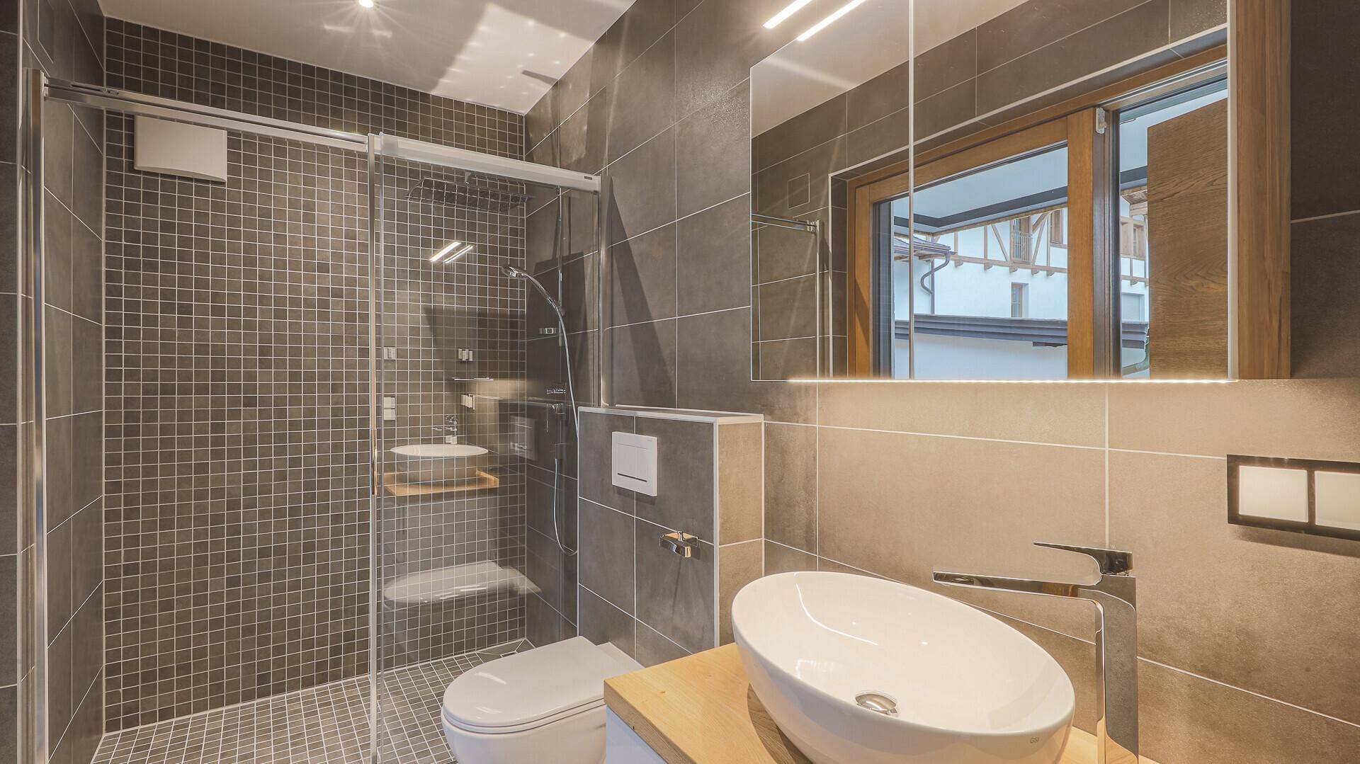 Modernes Badezimmer mit Dusche, Waschtisch, Wand-WC und beleuchtetem Spiegelschrank.
