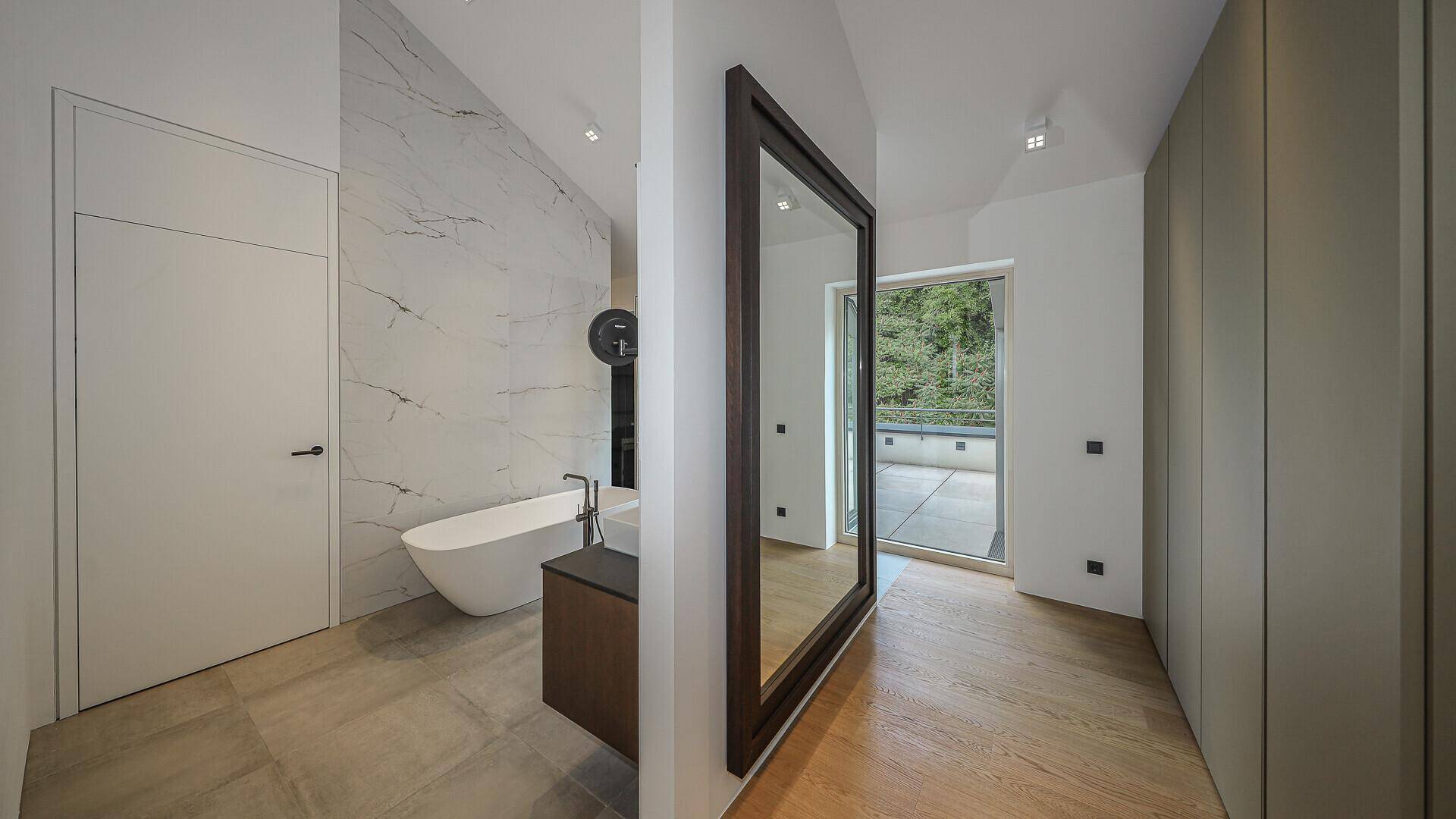 Luxuriöses Badezimmer mit freistehender Badewanne, Marmorwänden und Zugang zur Terrasse.