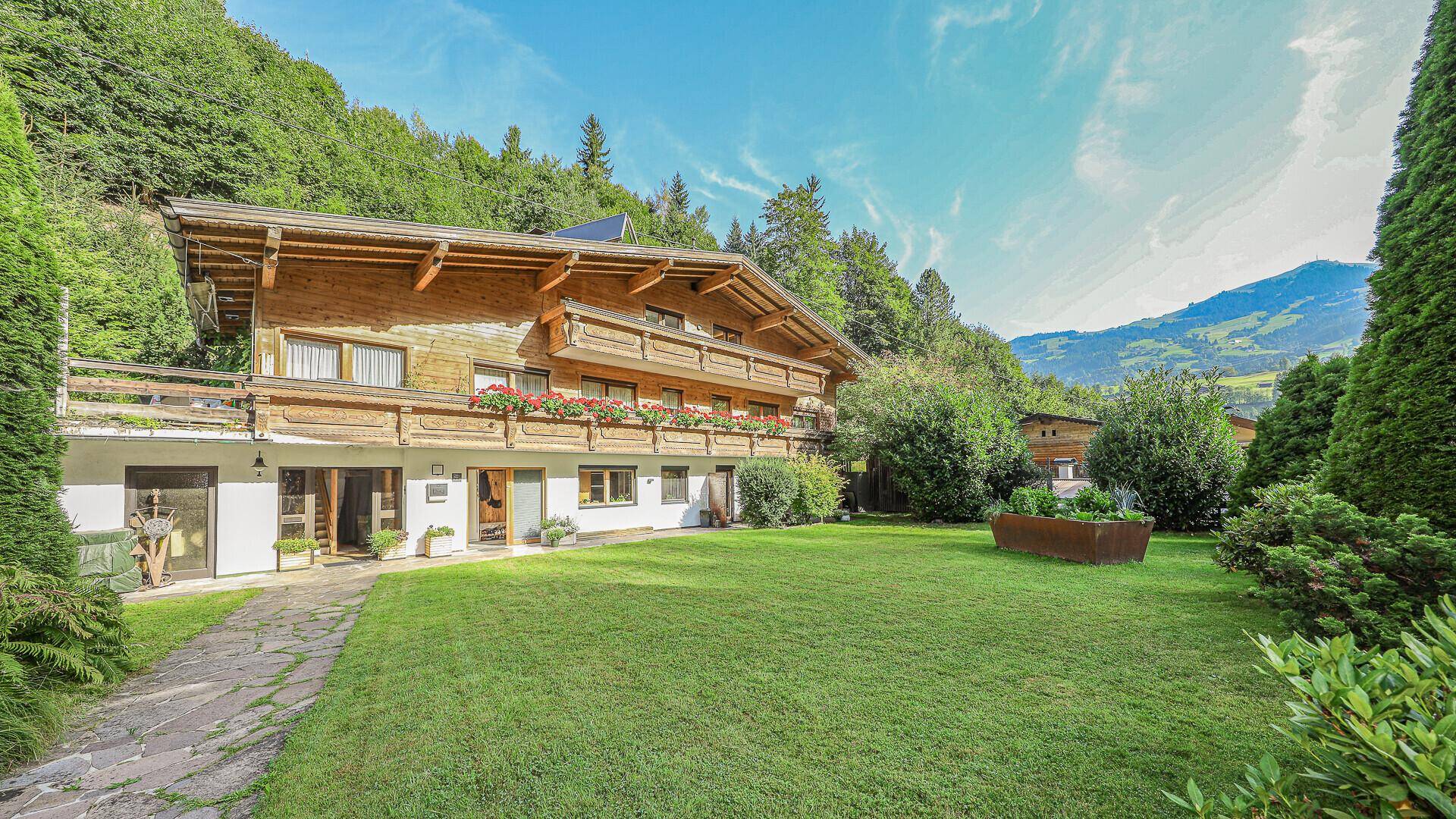 Traditionelles Holzhaus mit großem grünen Garten und Bergblick in alpiner Umgebung.