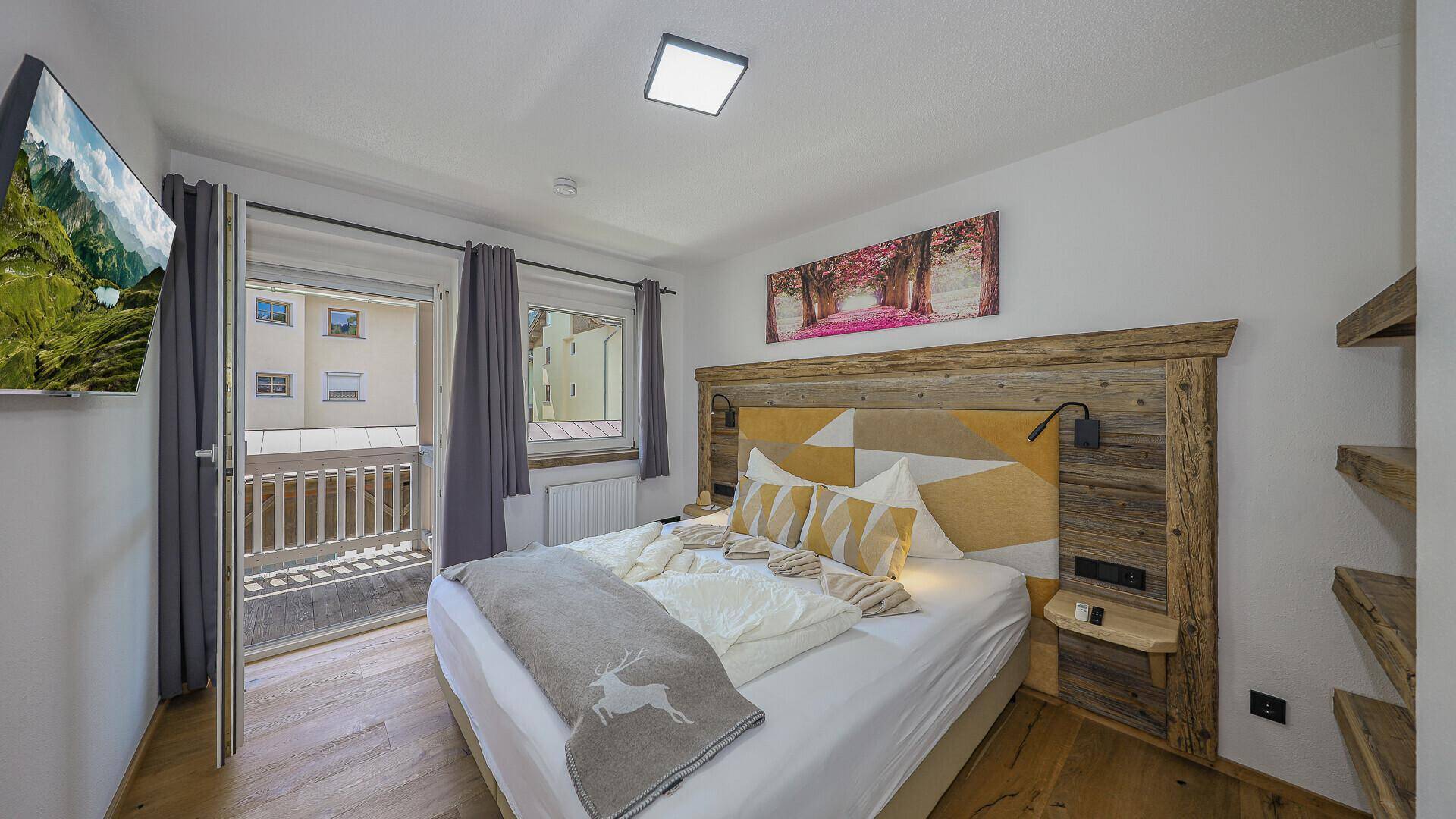 Gemütliches Schlafzimmer mit Doppelbett, Holzelementen und Zugang zu einem sonnigen Balkon.