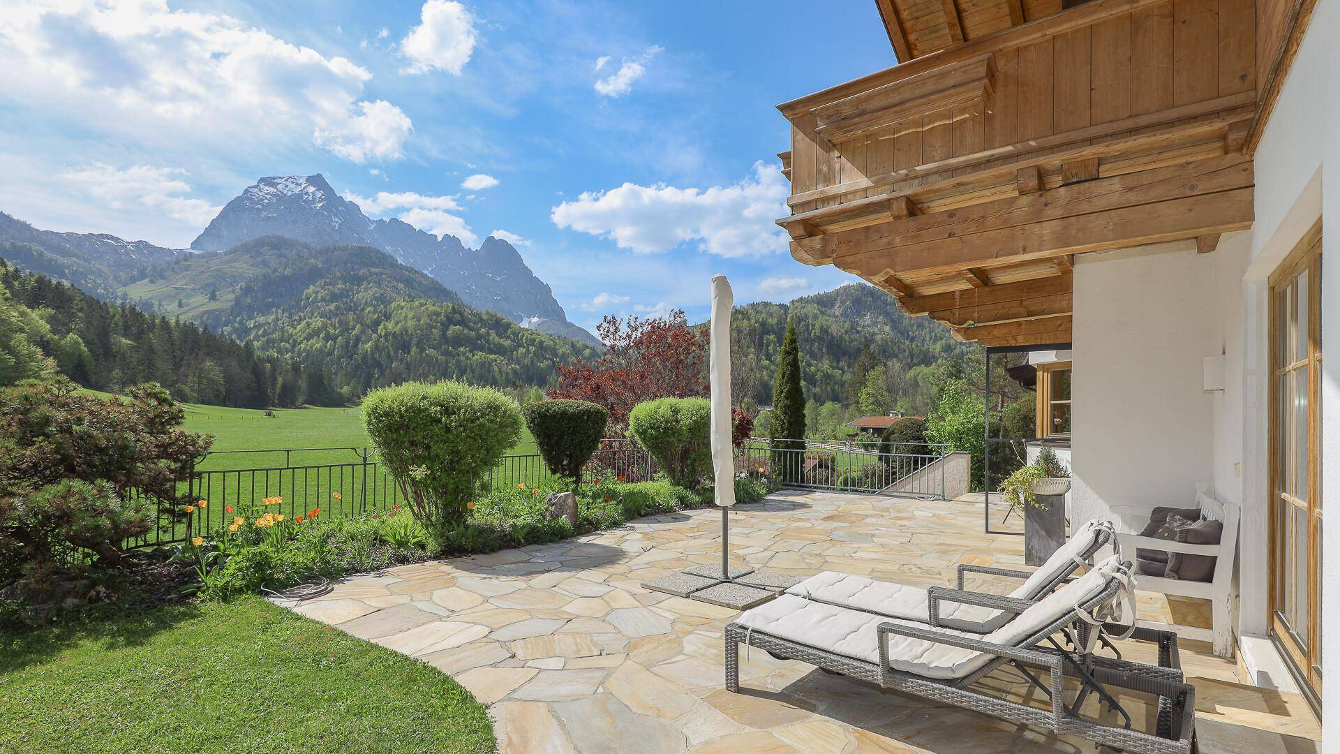 Sonnige Terrasse mit Liegestühlen, Steinfliesen und beeindruckendem Bergblick.