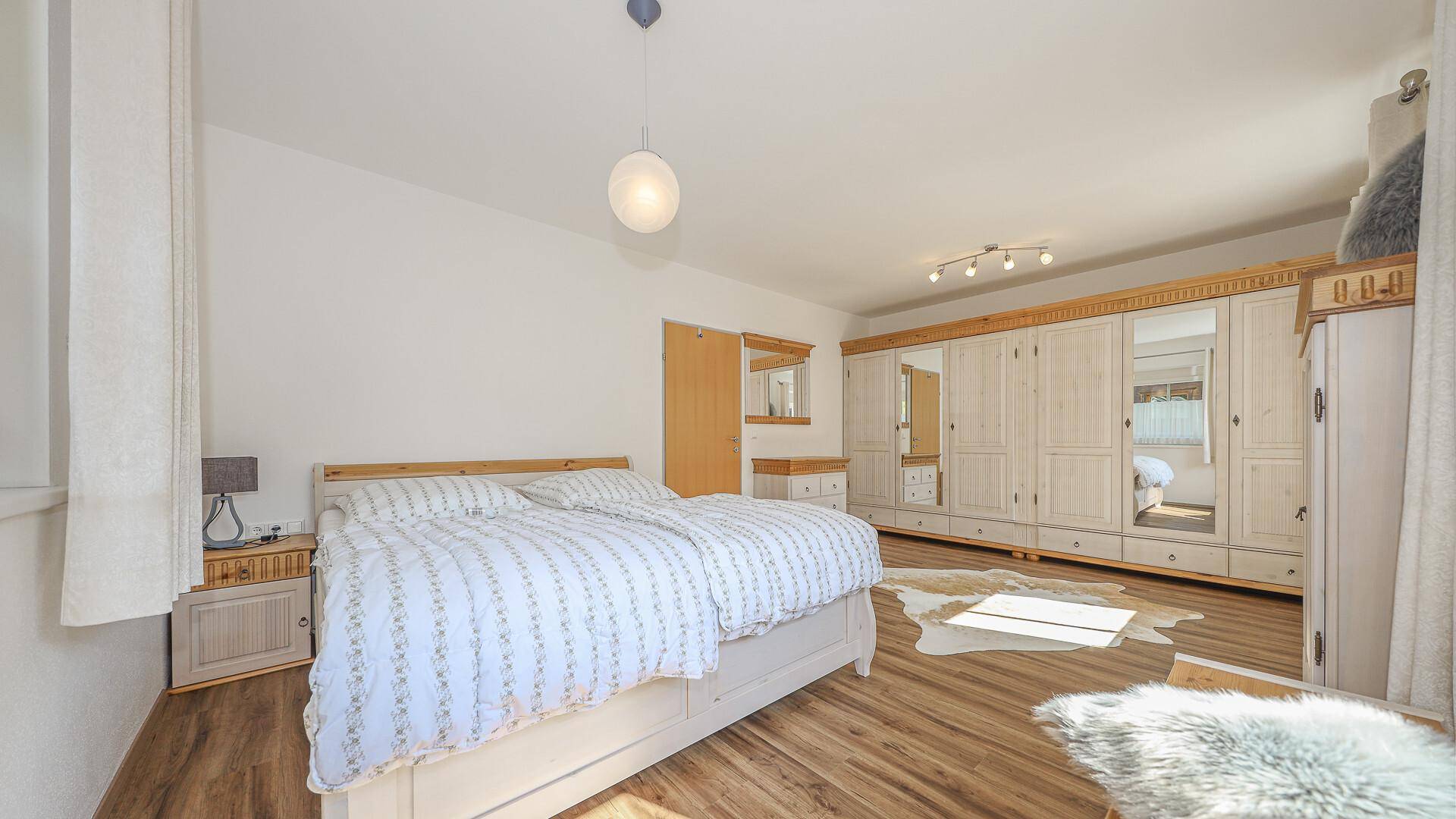Helles Schlafzimmer mit Holzboden, großem Kleiderschrank und traditionellen Möbeln.