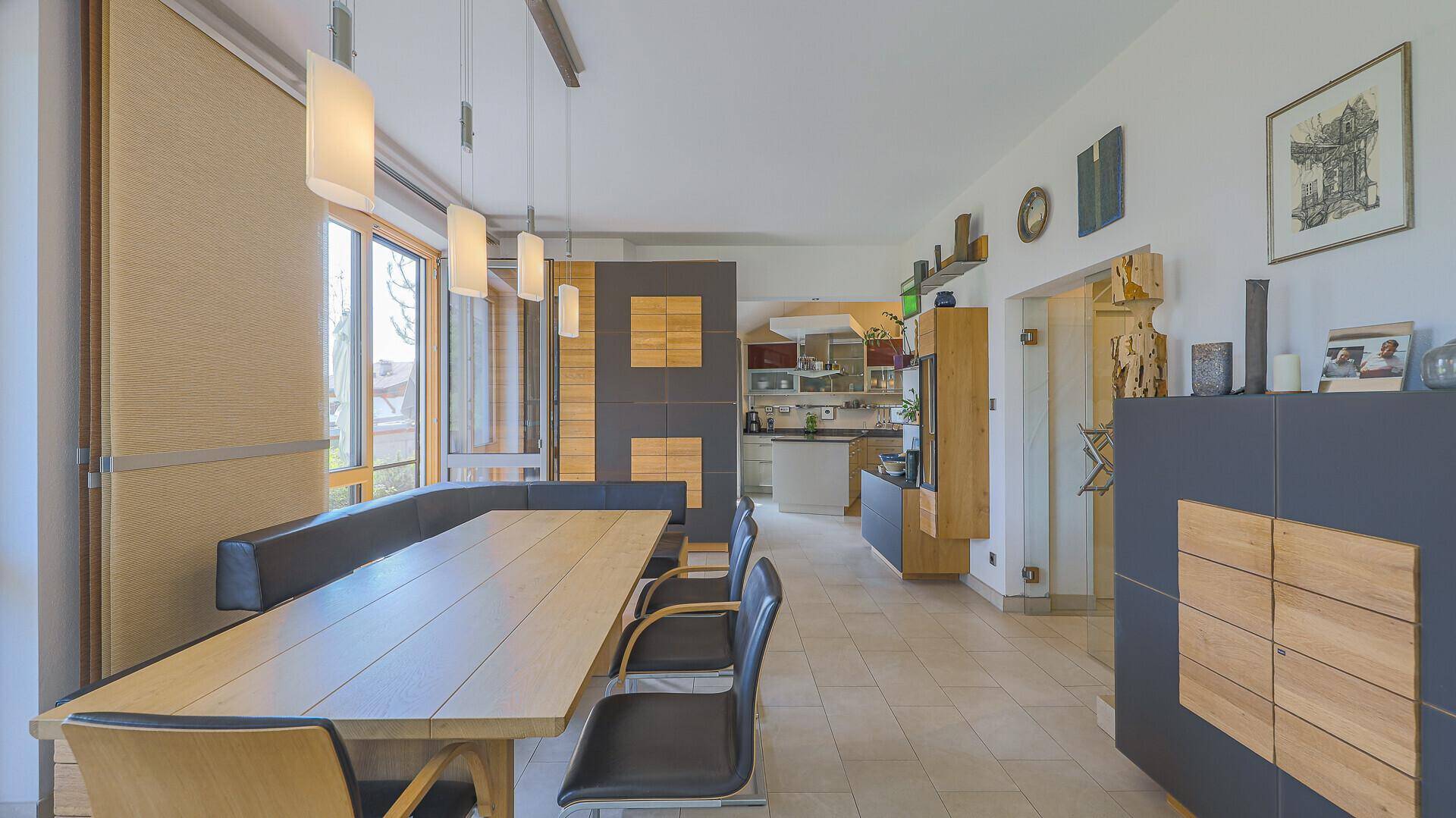 Essbereich mit Holztisch und Sitzbank, Fliesenboden und Blick in die angrenzende Küche.