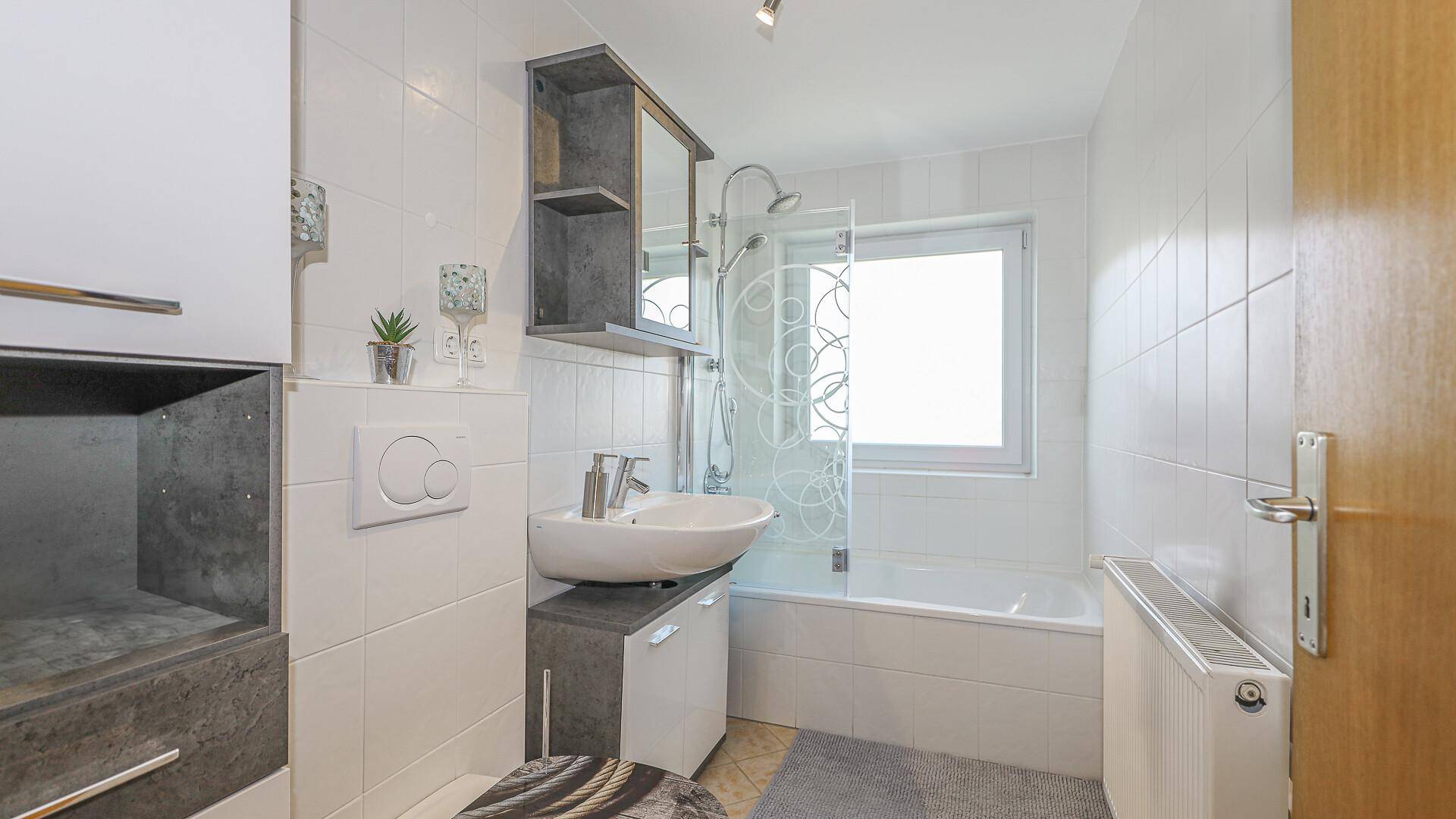 Badezimmer mit Badewanne, Dusche und Fenster, hell gefliest und gut beleuchtet.
