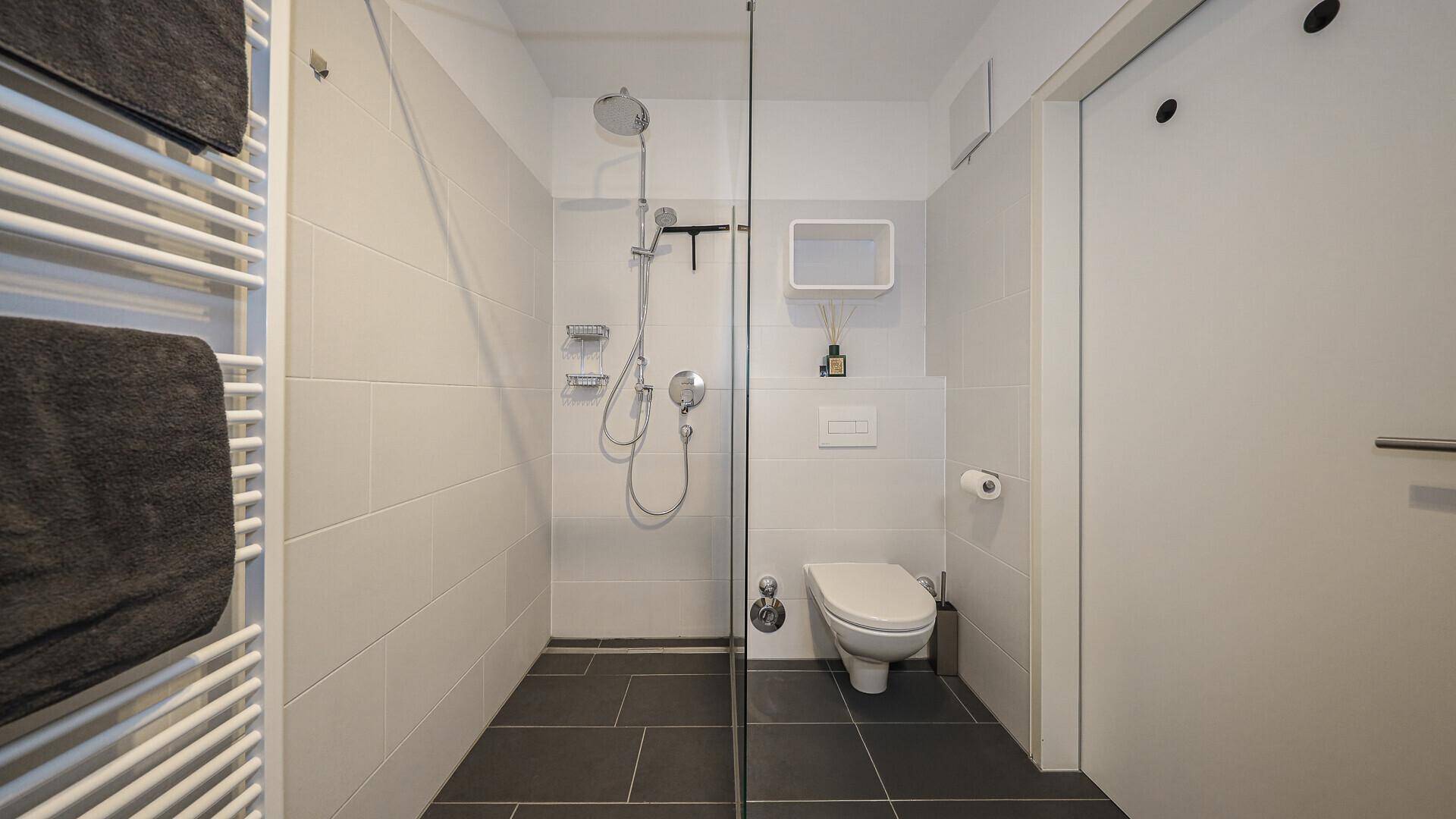 Modernes Badezimmer mit ebenerdiger Dusche, Wand-WC und beheiztem Handtuchhalter.