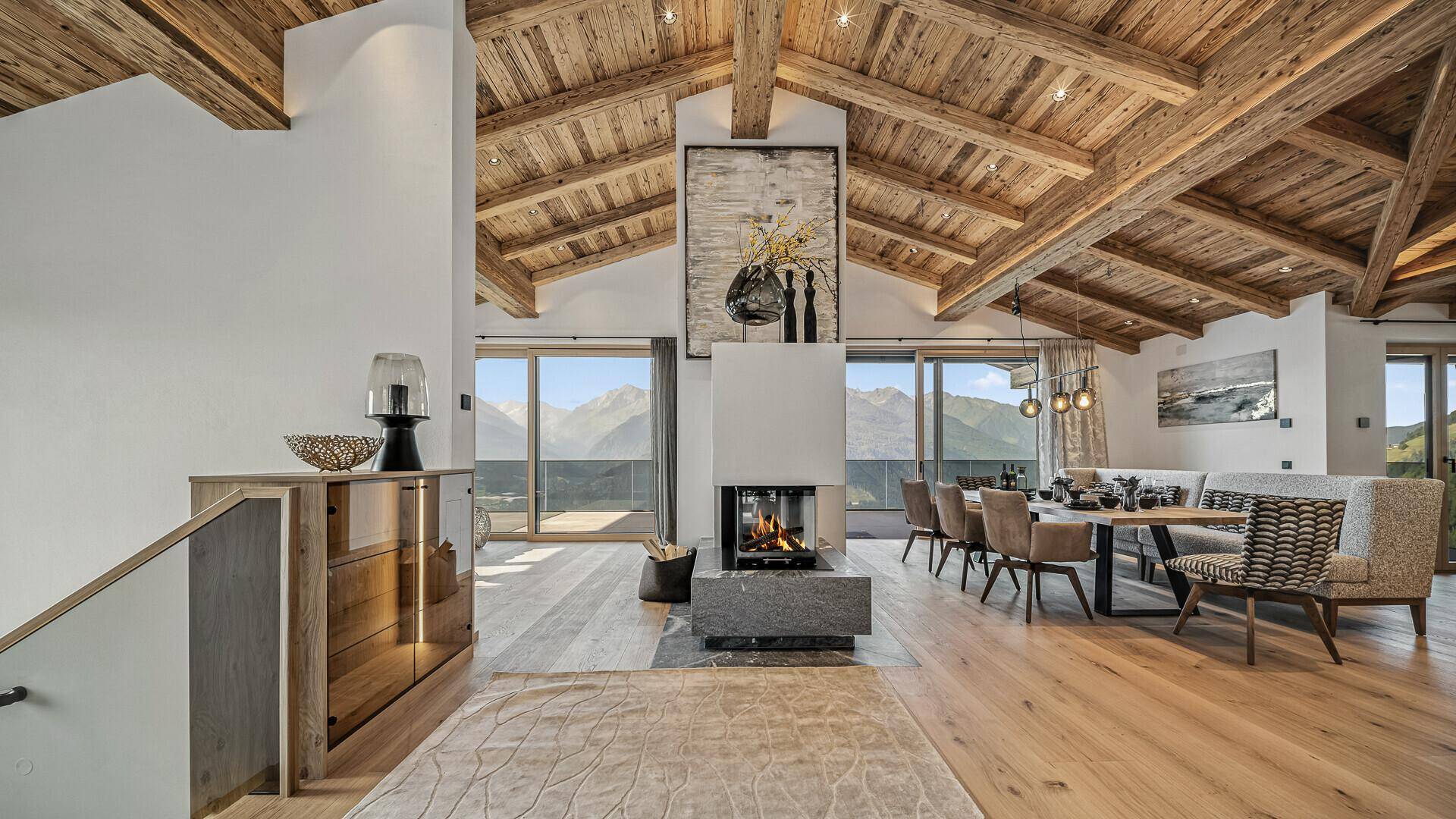 Geräumiger Wohn- und Essbereich mit Holzbalkendecke, Kamin und Panoramablick auf die Berge.