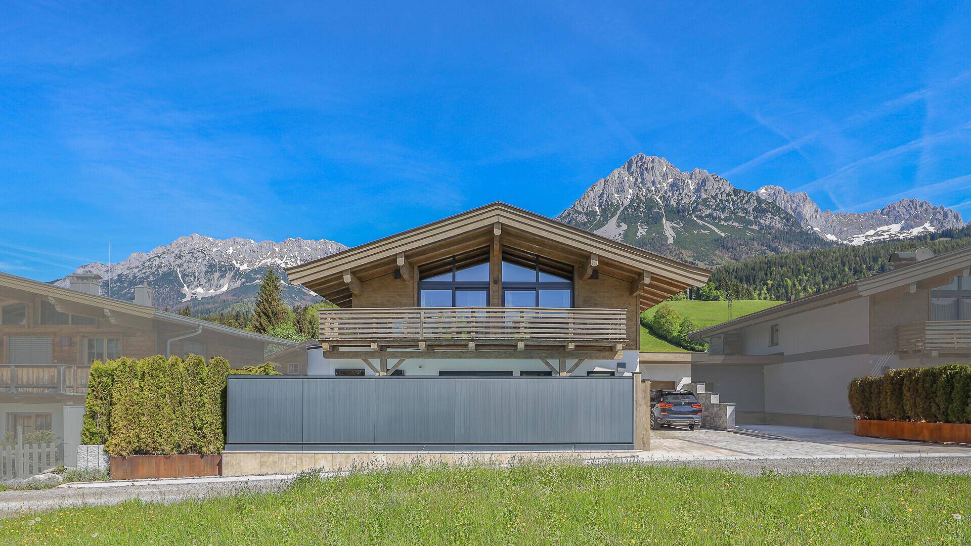Moderne Chalet-Fassade mit Holzelementen, großem Balkon und beeindruckendem Bergblick.