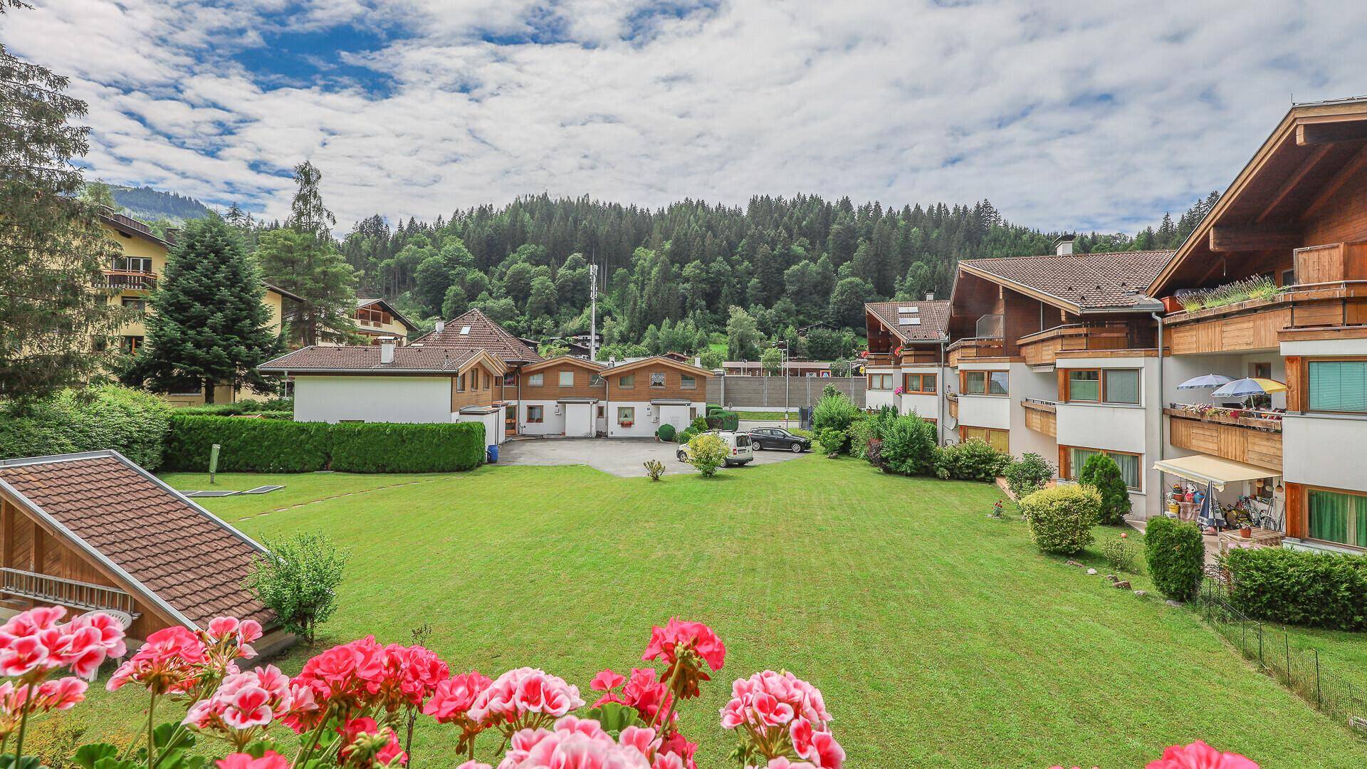 Weitläufiger Blick vom Balkon über eine grüne Wiese, umliegende Häuser und Berge.
