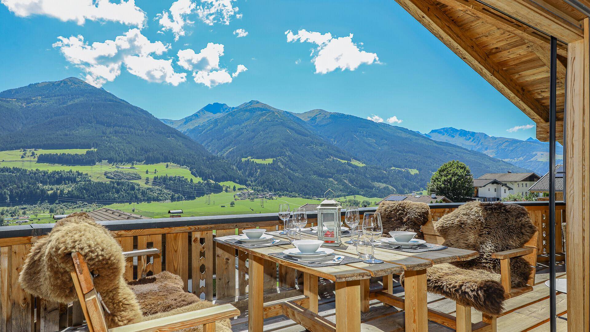 Sonnenterrasse mit Esstisch und Stühlen, umgeben von einer atemberaubenden Bergkulisse.