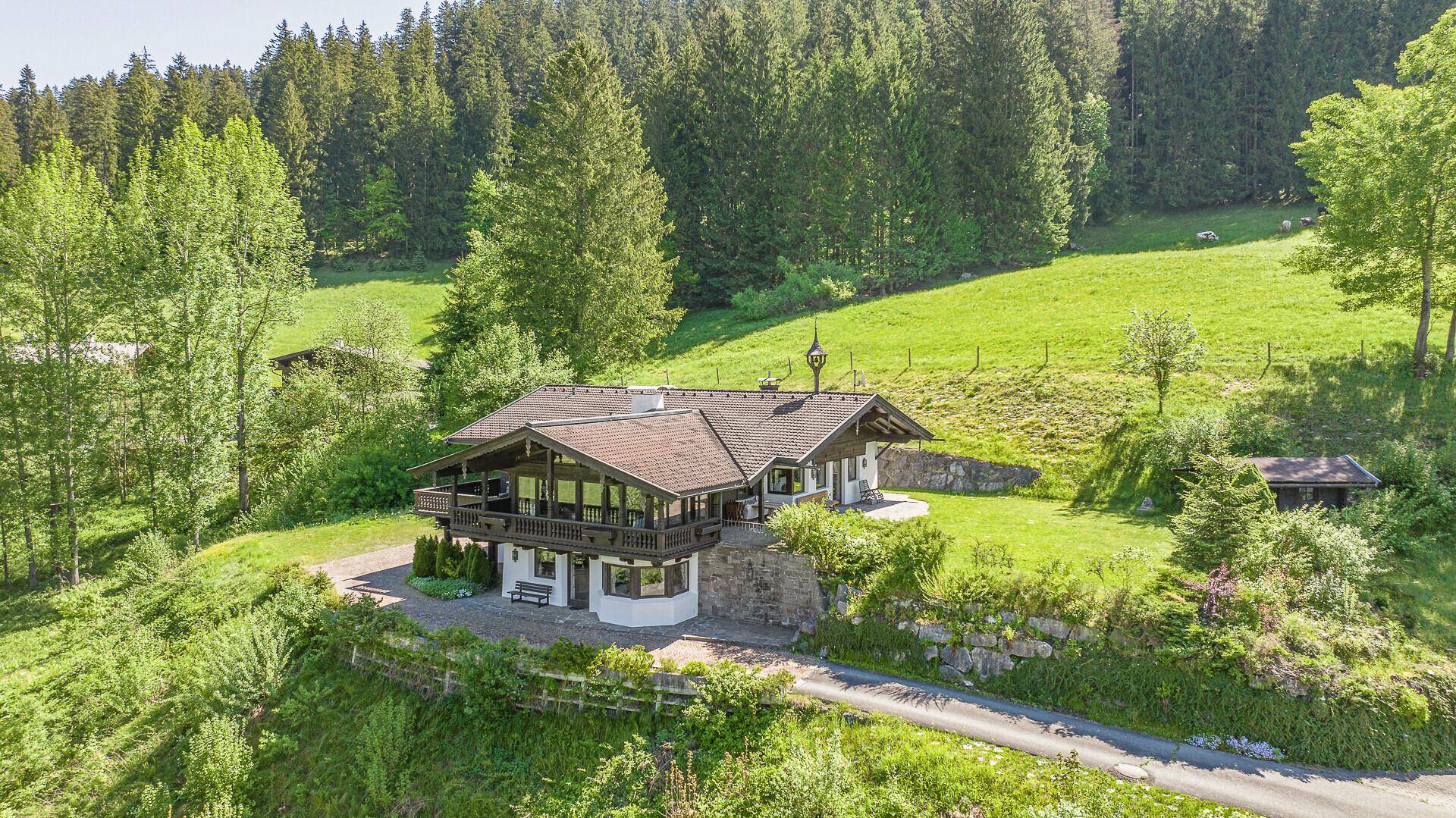 Traditionelles Alpenhaus in sonniger Lage, umgeben von grünen Wiesen und Wäldern.