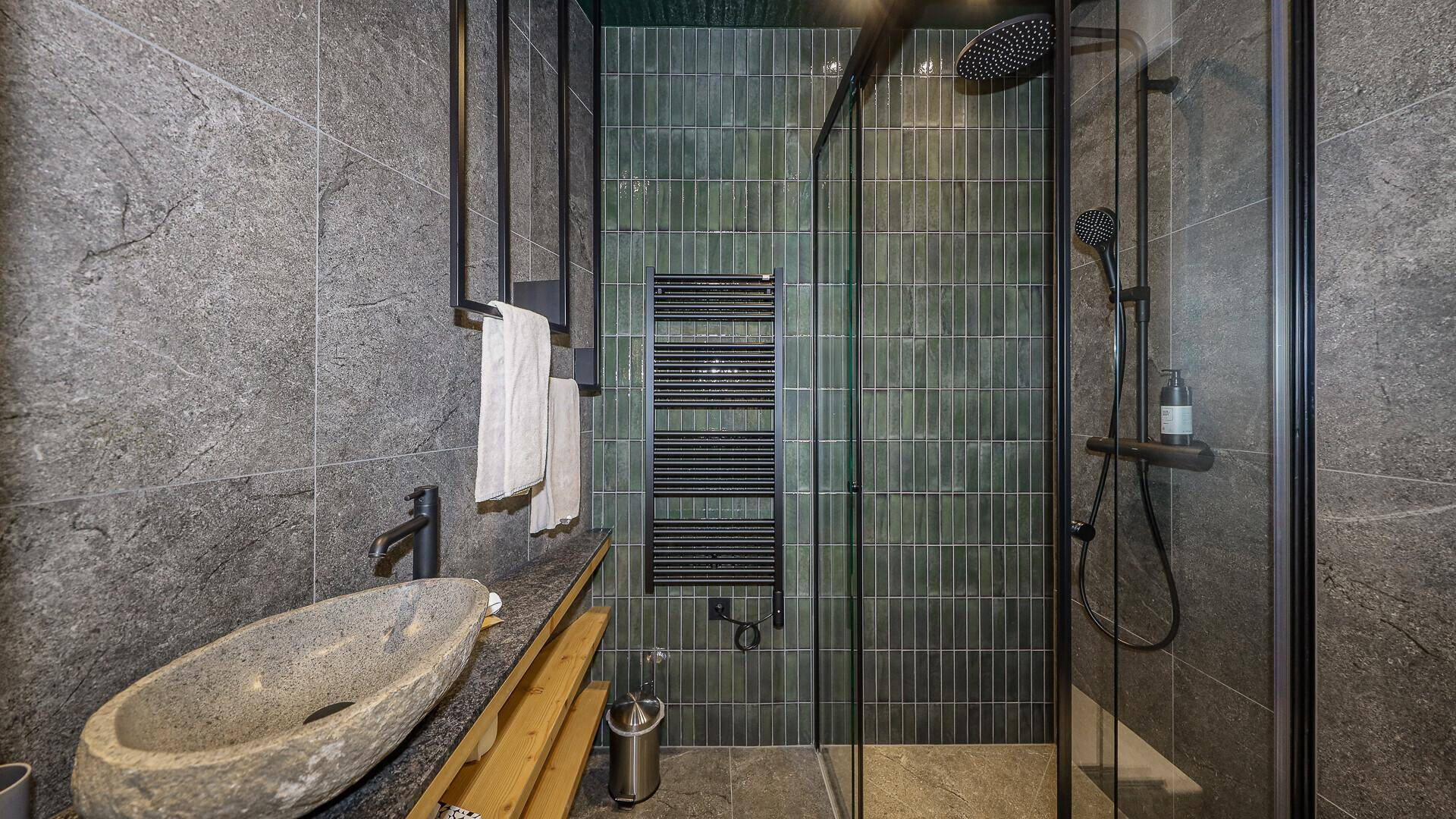 Elegantes Badezimmer mit dunklen Fliesen, Natursteinwaschbecken und moderner Duschkabine.