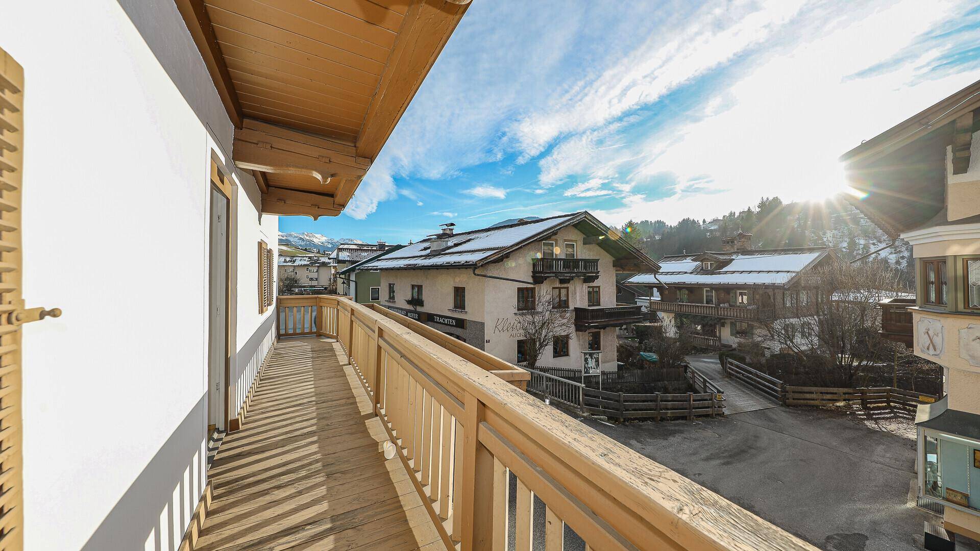 Langer Holzbalkon mit Blick auf die umliegende Berglandschaft und das Dorf.