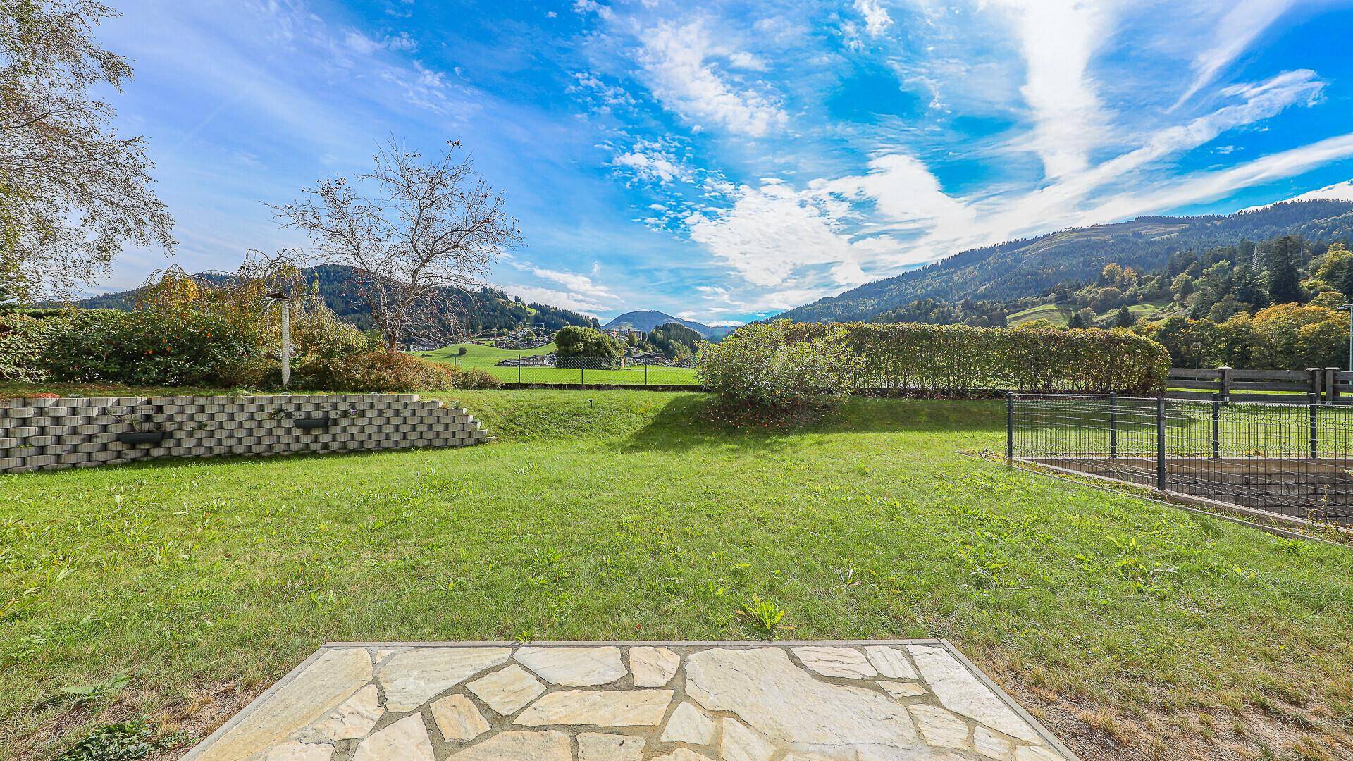 Weitläufiger Garten mit Rasenfläche und Panoramablick auf die grüne Berglandschaft unter blauem Himmel.