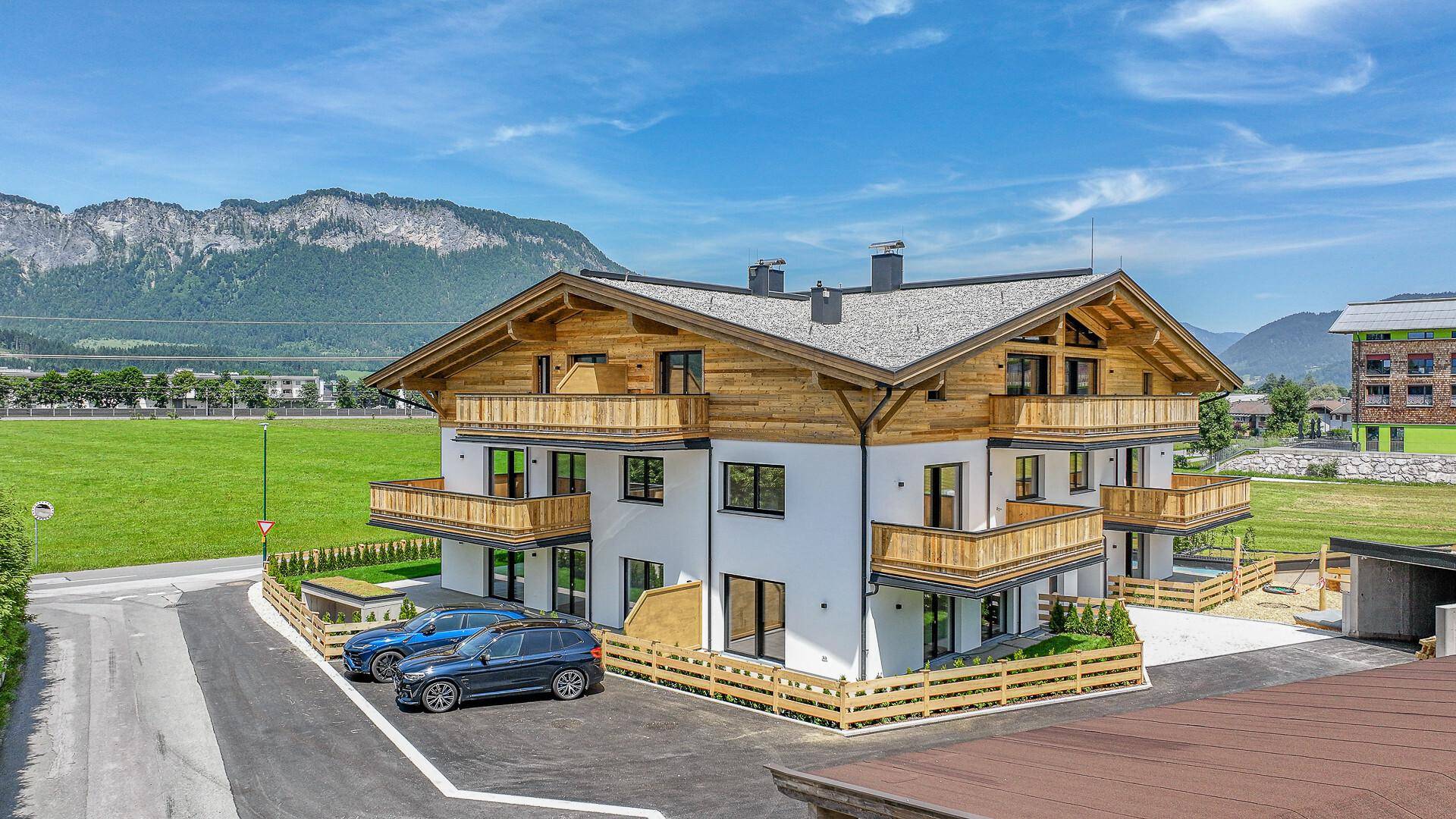 Neubau-Wohnhaus mit Parkplätzen und traditionellen Holzbalkonen in ländlicher Umgebung.