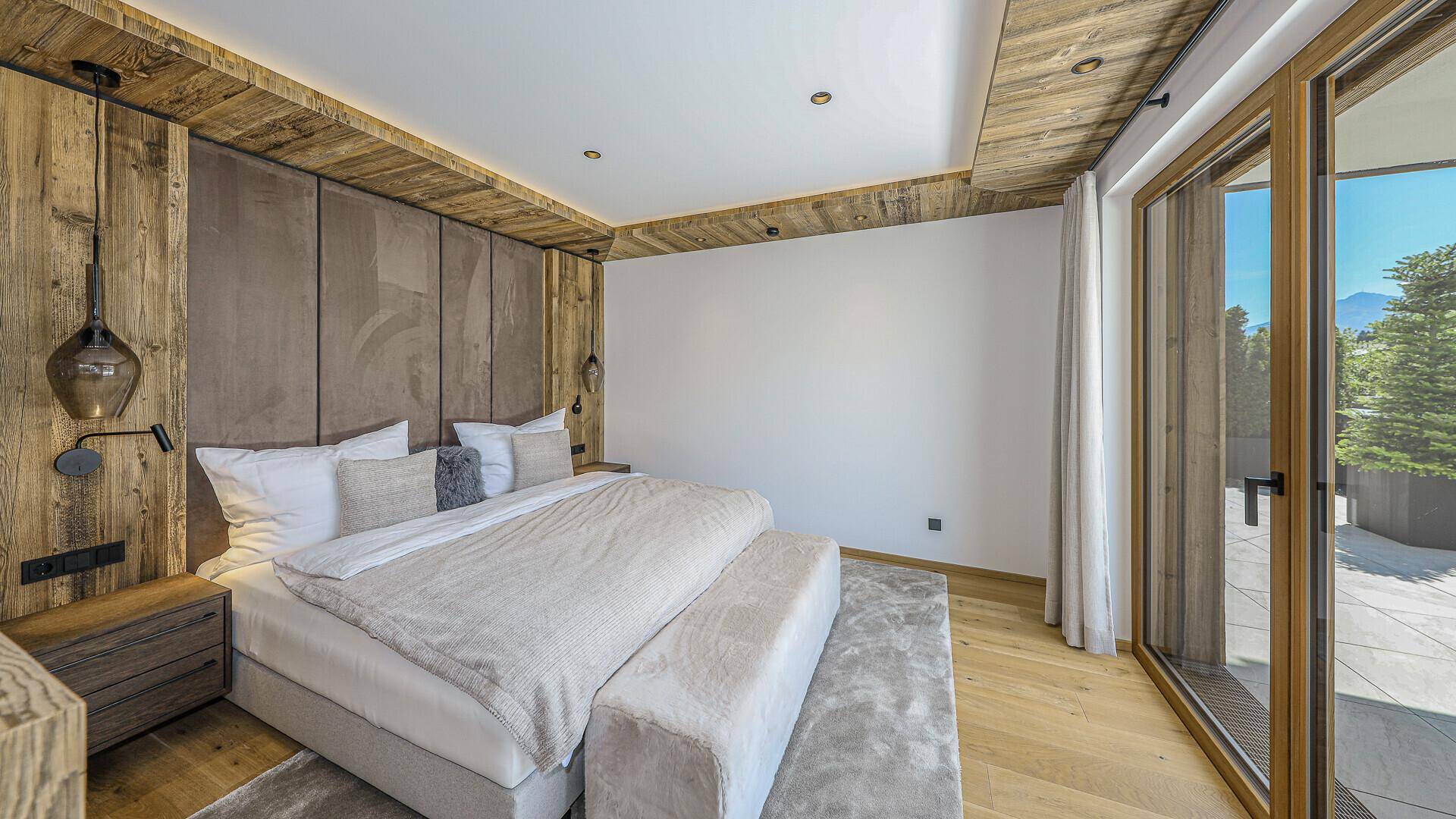 Helles Schlafzimmer mit Holzboden, großen Fenstern und Zugang zu einem Außenbereich.