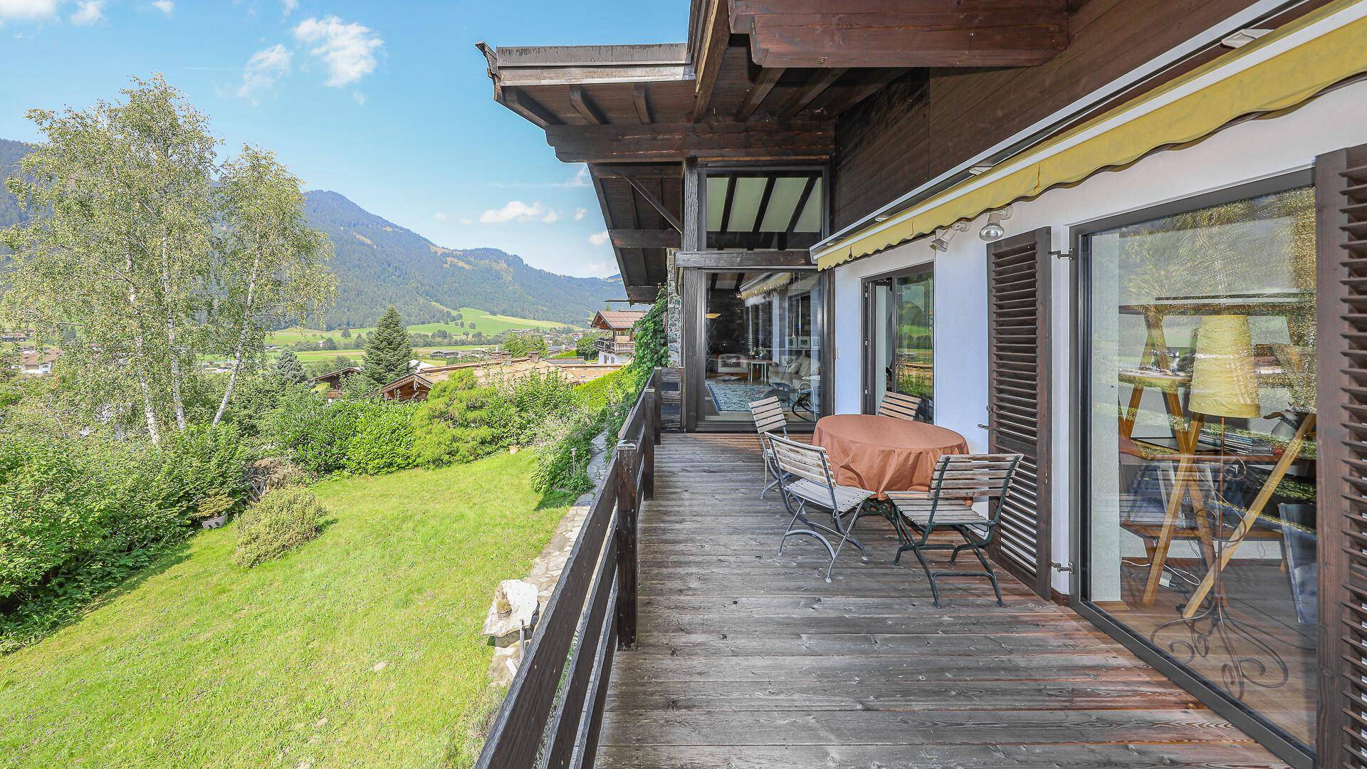 Geräumiger Holzbalkon mit Sitzgelegenheiten und weitem Blick auf die grüne Berglandschaft.