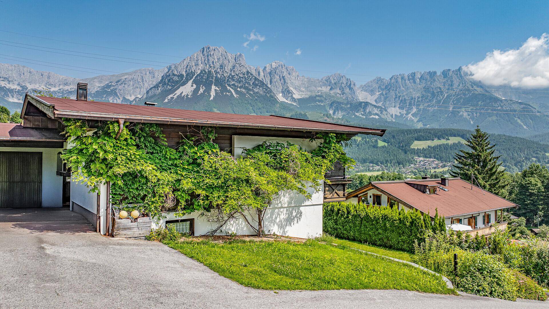 Traditionelles Haus mit üppiger Kletterpflanze und Garage vor beeindruckender Bergkulisse.