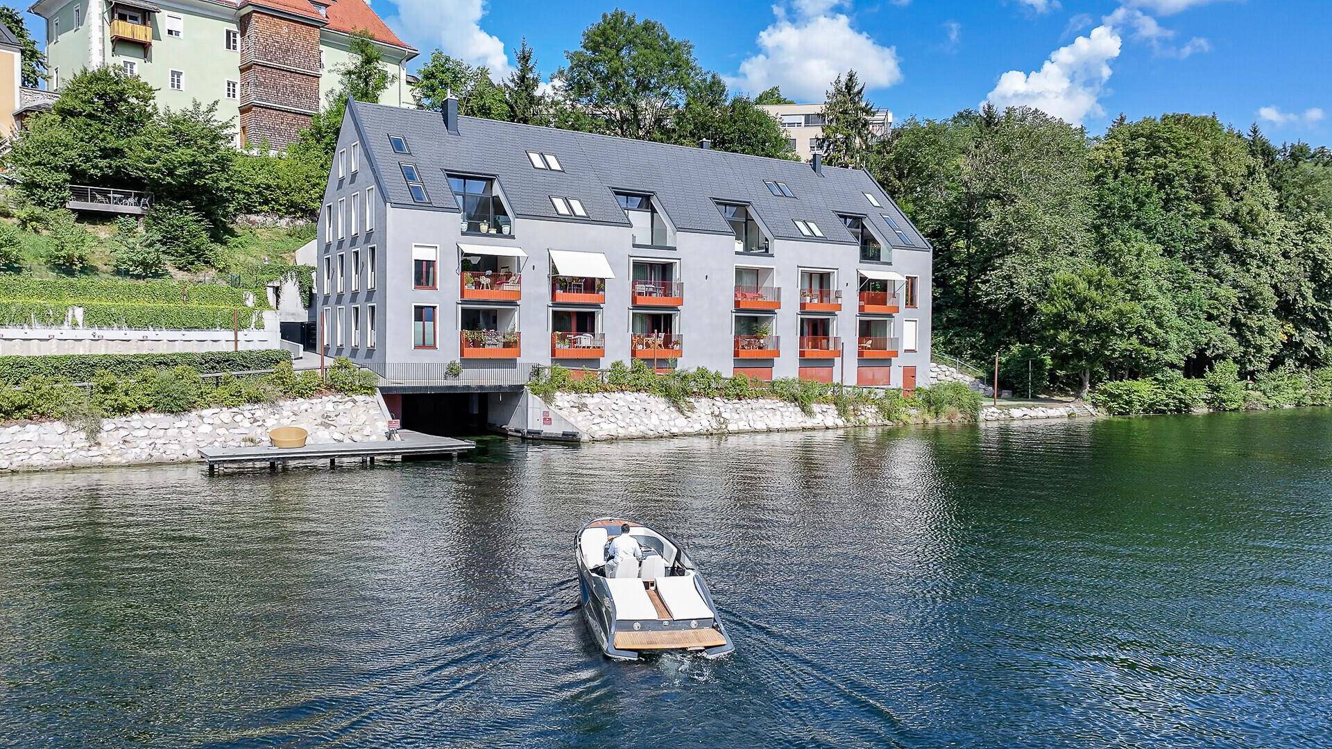 Ansicht des modernen Gebäudes vom Wasser aus, mit Balkonen und Dachfenstern.
