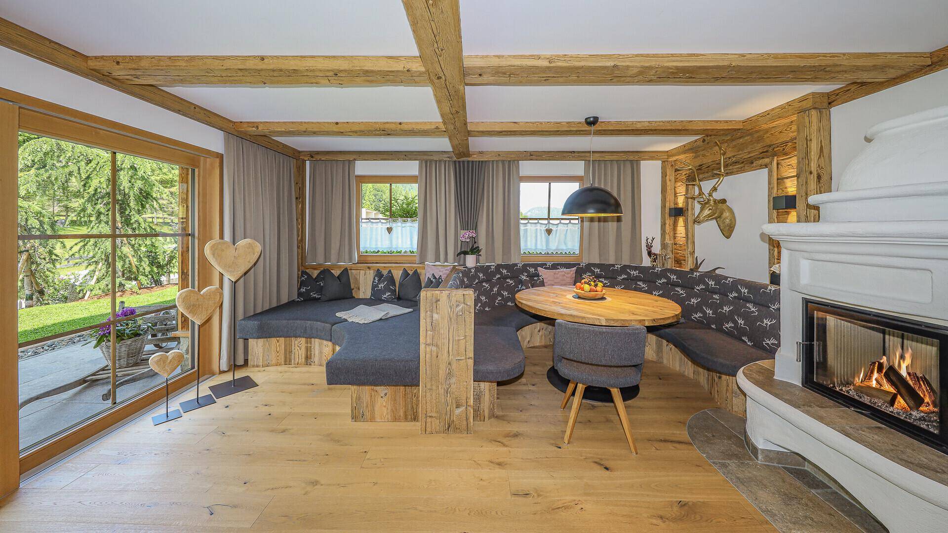 Helles Wohnzimmer mit Holzbalkendecke, Kamin und großer Fensterfront zum Garten.