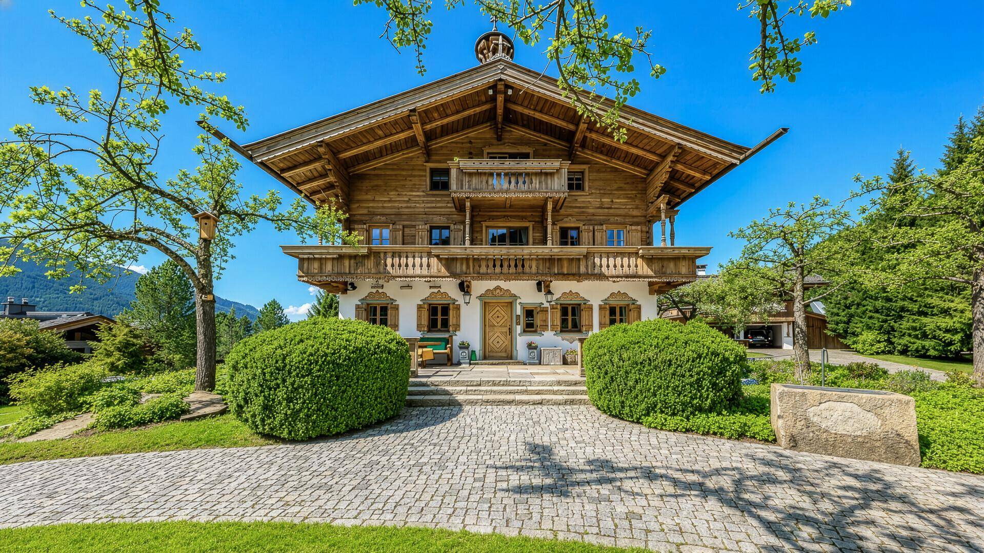 Traditionelles Alpenchalet mit Holzbalkonen, gepflegtem Vorgarten und gepflasterter Auffahrt.