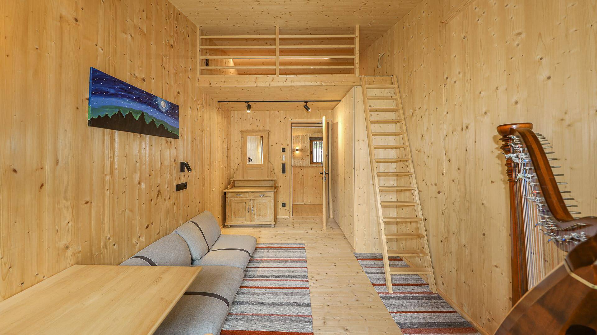 Heller Wohnbereich mit Sofa, Holzwänden und einem Hochbett, ideal für Gäste oder als Spielzimmer.