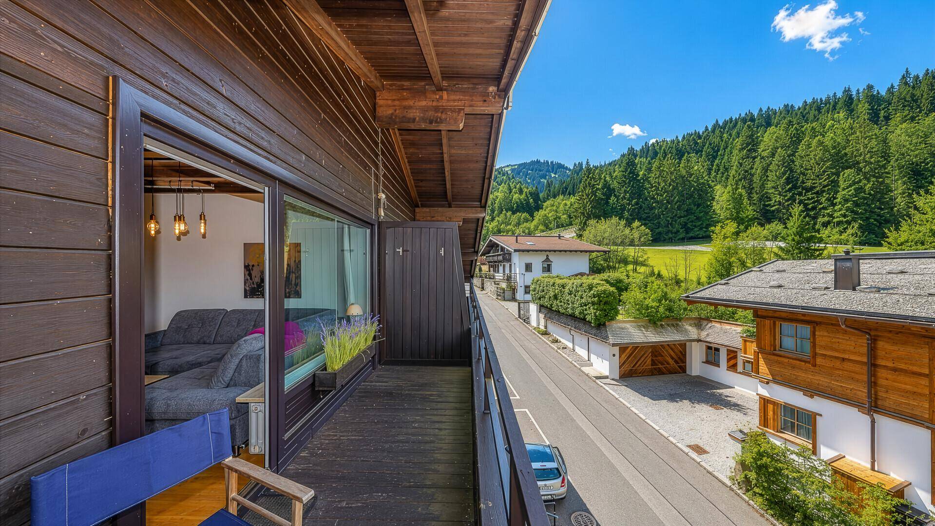 Langer Holzbalkon mit Blick auf die Straße und die umliegende grüne Berglandschaft.