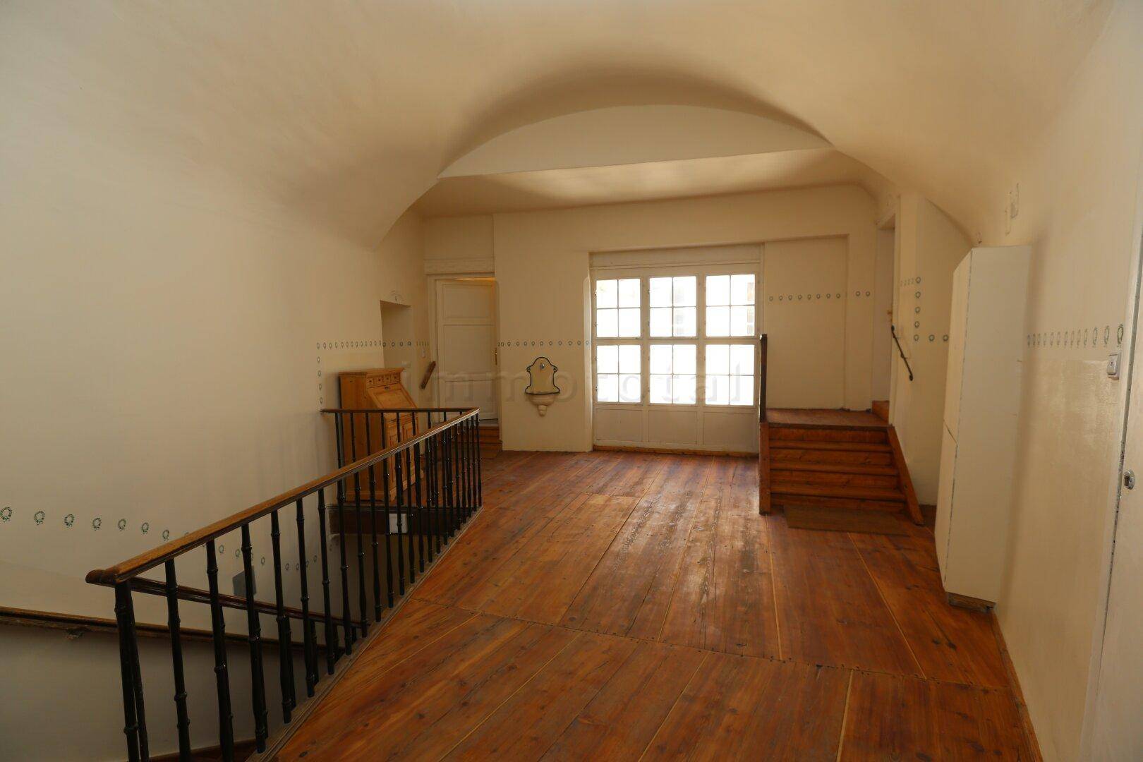Heller Flur mit gewölbter Decke, breiten Holzplanken und Zugang zu weiteren Räumen über eine Treppe.