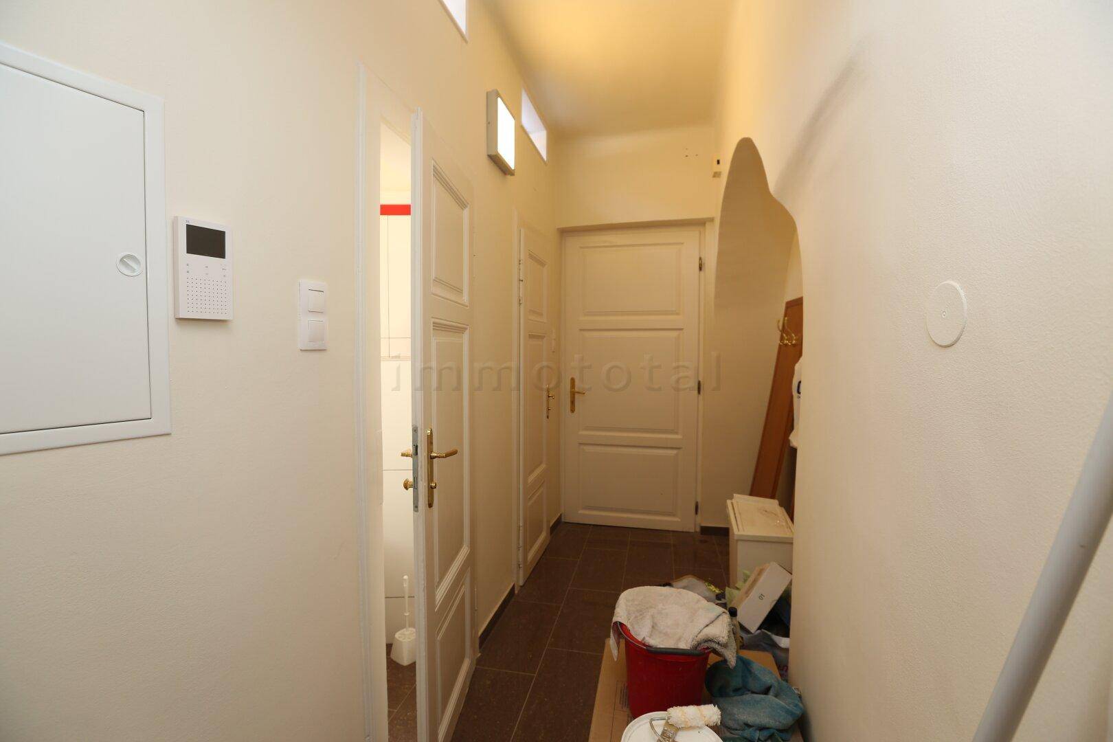 Langer Flur mit mehreren Türen und Zugang zu einem Badezimmer, ausgestattet mit Fliesenboden.