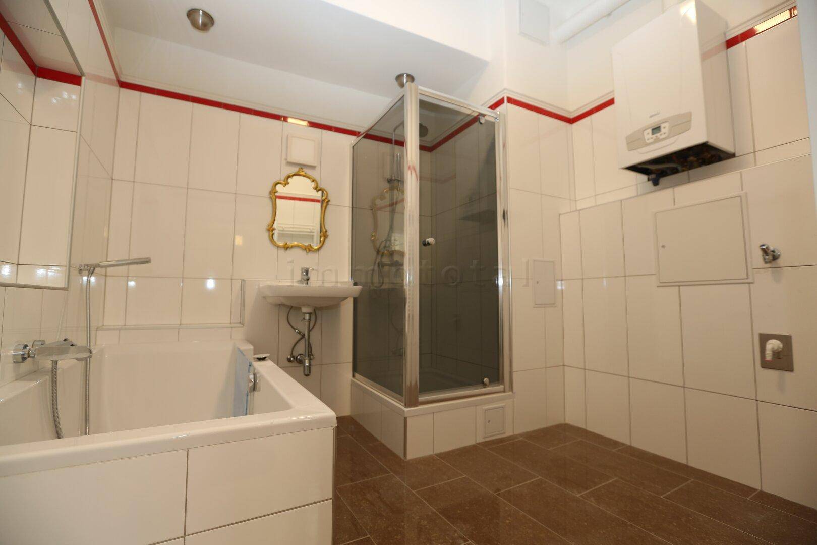 Badezimmer mit Badewanne, Duschkabine, Waschbecken und Gastherme, ausgestattet mit weißen Fliesen und roten Akzenten.