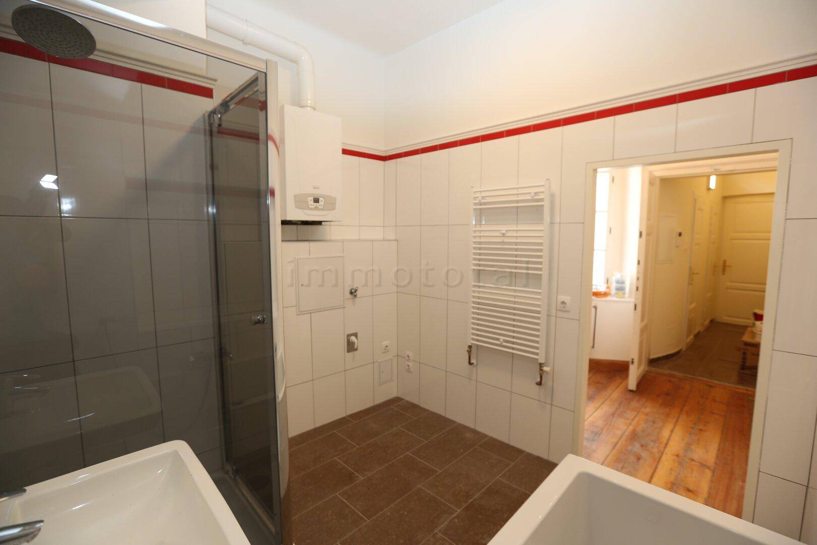 Badezimmer mit Duschkabine, beheiztem Handtuchhalter und Zugang zu einem Raum mit Holzplankenboden.