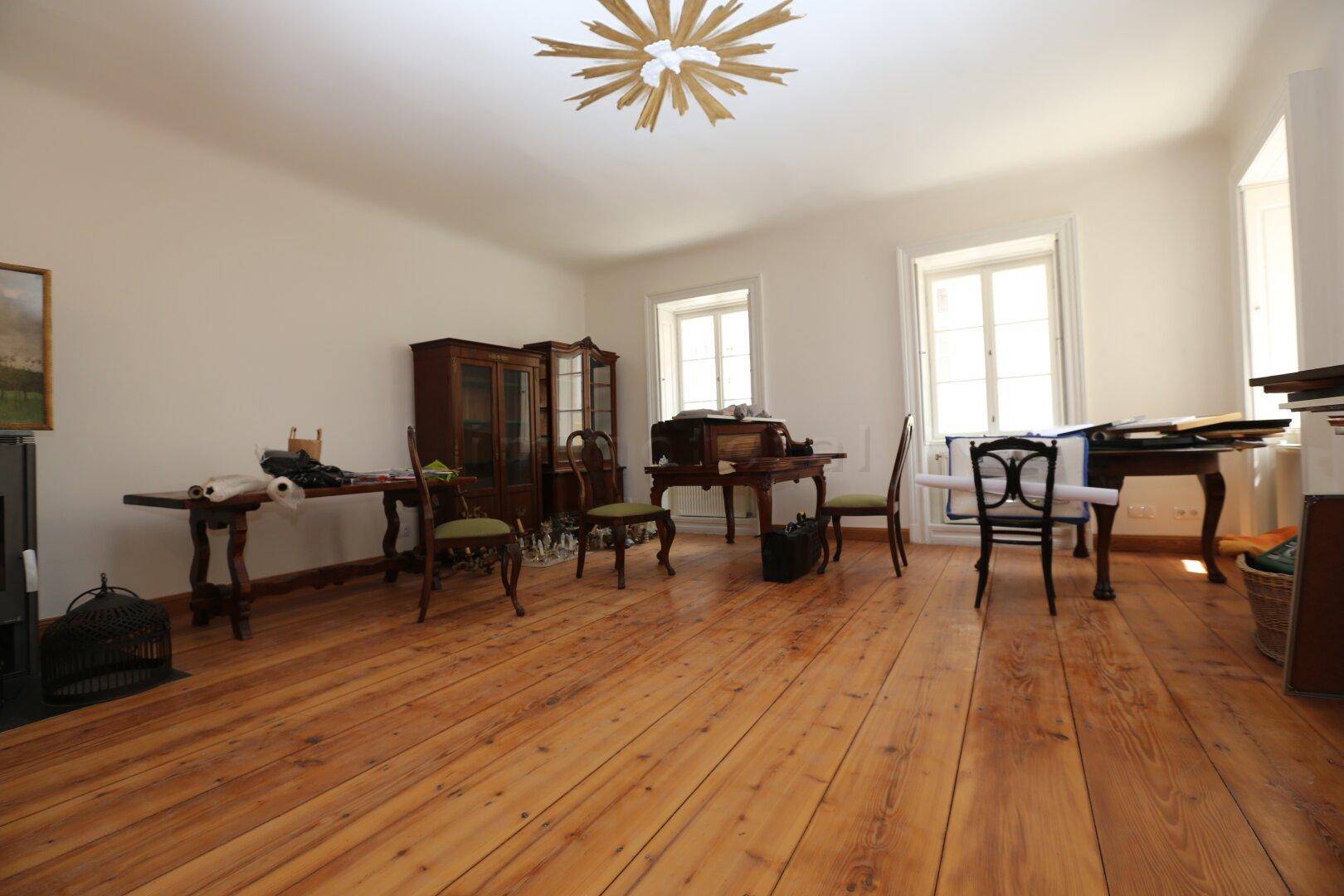 Großes Wohnzimmer mit breiten Holzplanken, hohen Fenstern und klassischem Mobiliar.