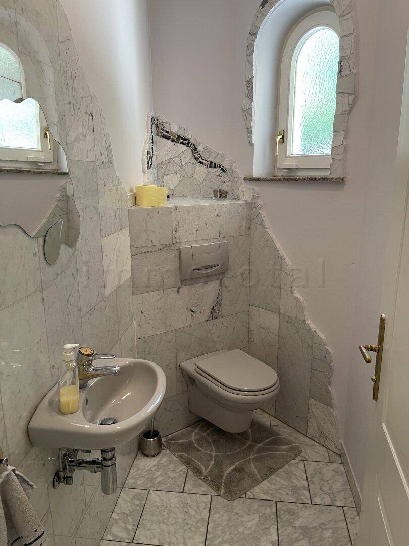 Elegantes Gäste-WC mit Marmorfliesen, wandhängendem WC und einem kleinen Fenster.