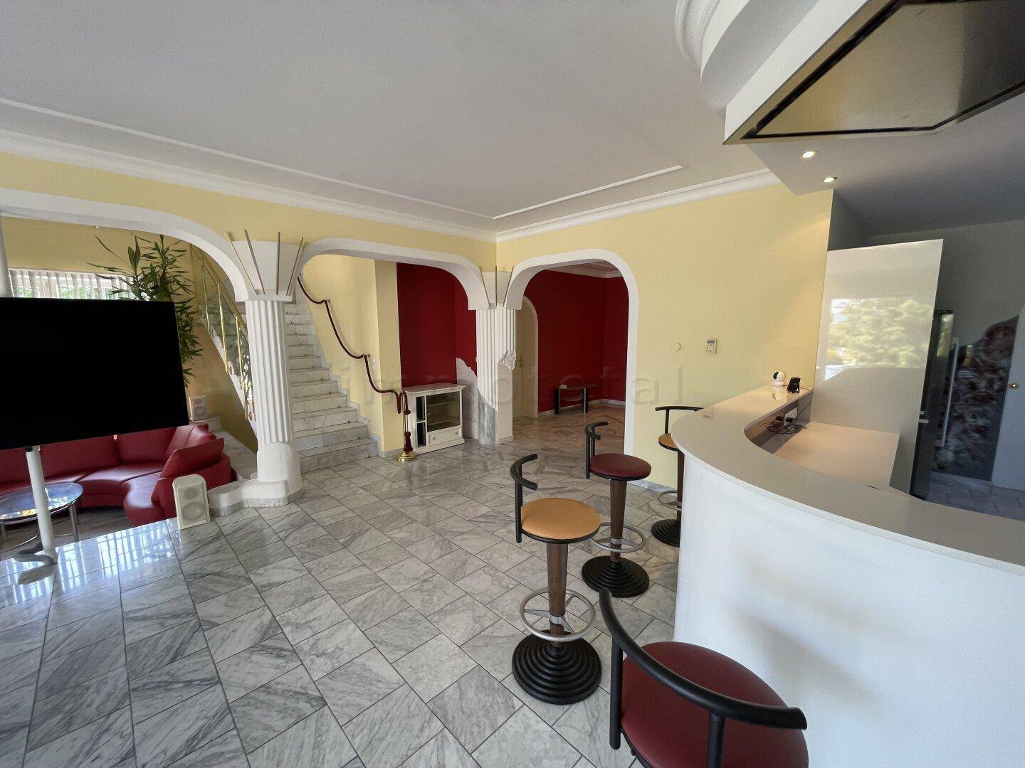 Großzügiger Wohnbereich mit Bar, Marmorfliesen und einer eleganten Treppe zum Obergeschoss.