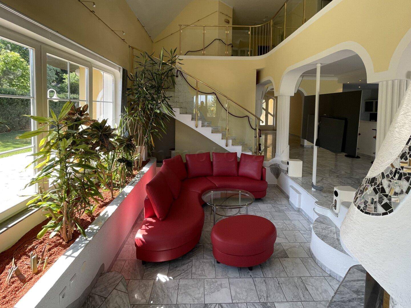 Heller Wohnbereich mit rotem Sofa, großen Fenstern und Blick in den grünen Garten.
