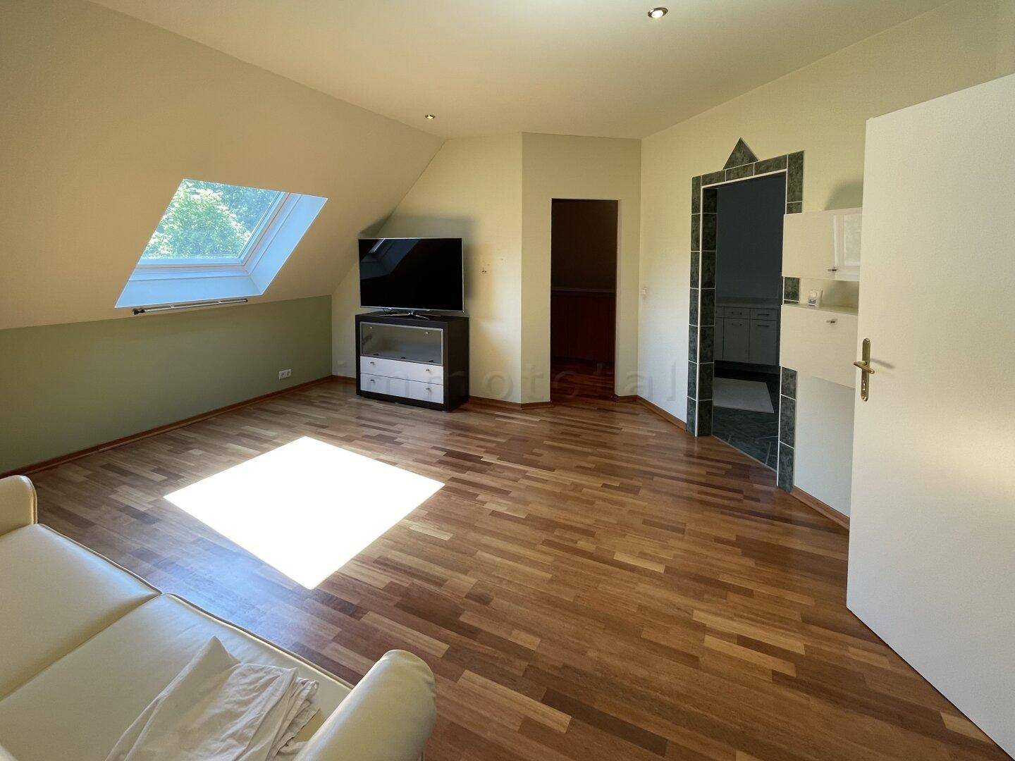 Helles Schlafzimmer im Dachgeschoss mit Holzboden, Dachfenster und schrägen Wänden.