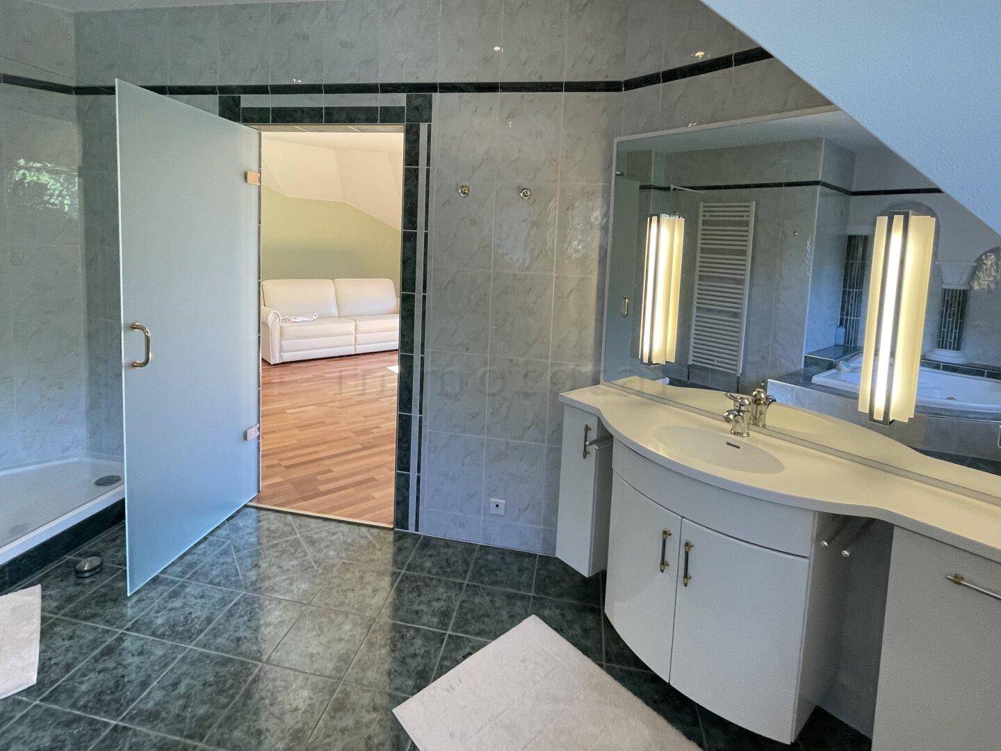 Modernes Badezimmer mit Einzelwaschbecken, großem Spiegel und Zugang zu einem angrenzenden Raum.