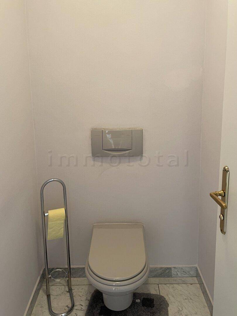 Einfaches WC mit wandhängender Toilette und hellen Fliesen.