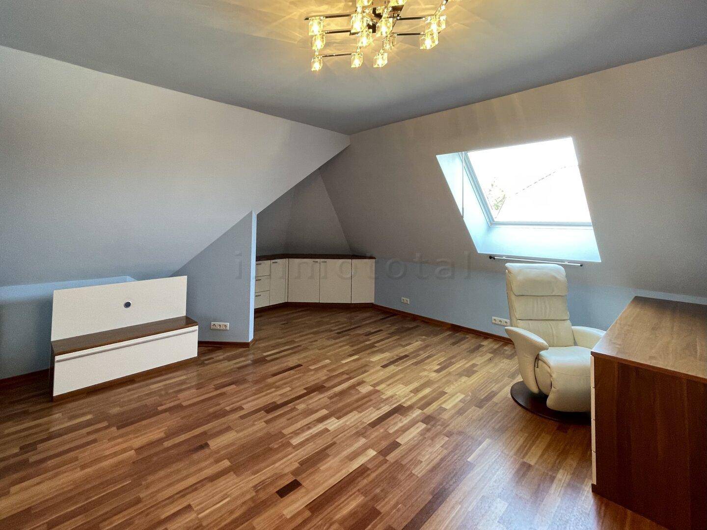 Helles Dachgeschosszimmer mit Holzboden, Dachfenster und integrierten Stauräumen.