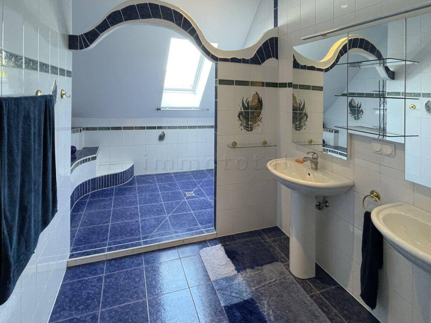 Geräumiges Badezimmer im Dachgeschoss mit blauen Fliesen, Dusche und Dachfenster.