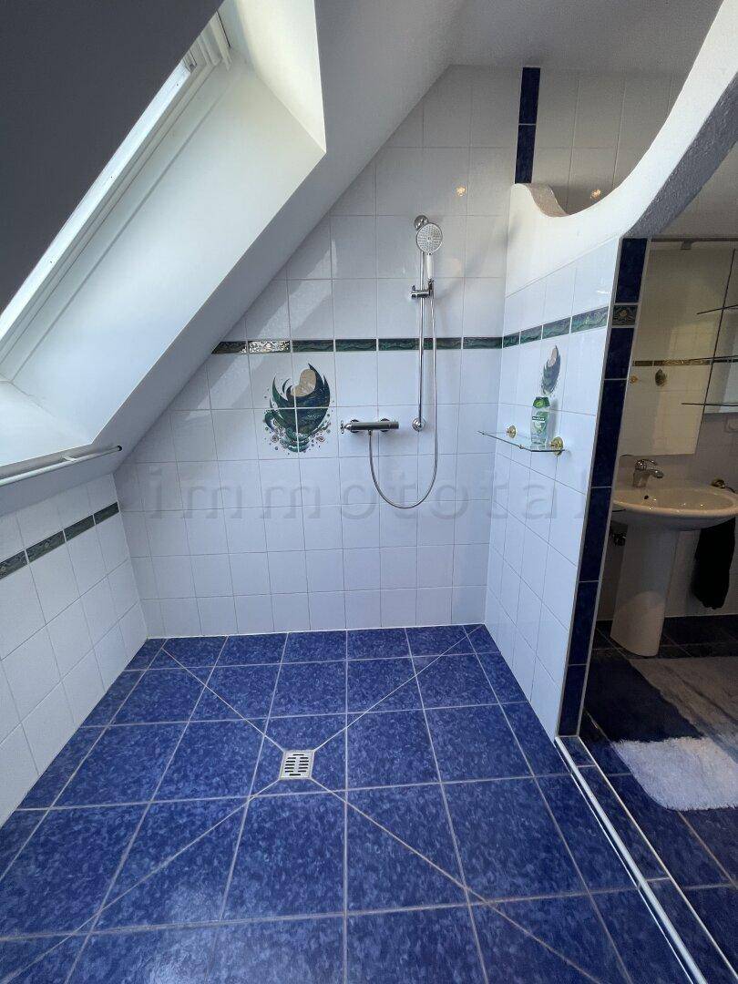 Große Duschkabine im Dachgeschoss mit blauen Fliesen und viel Tageslicht durch das Dachfenster.