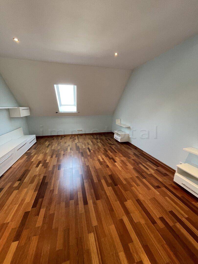Helles Dachgeschosszimmer mit Holzboden, Dachfenster und schrägen Wänden.