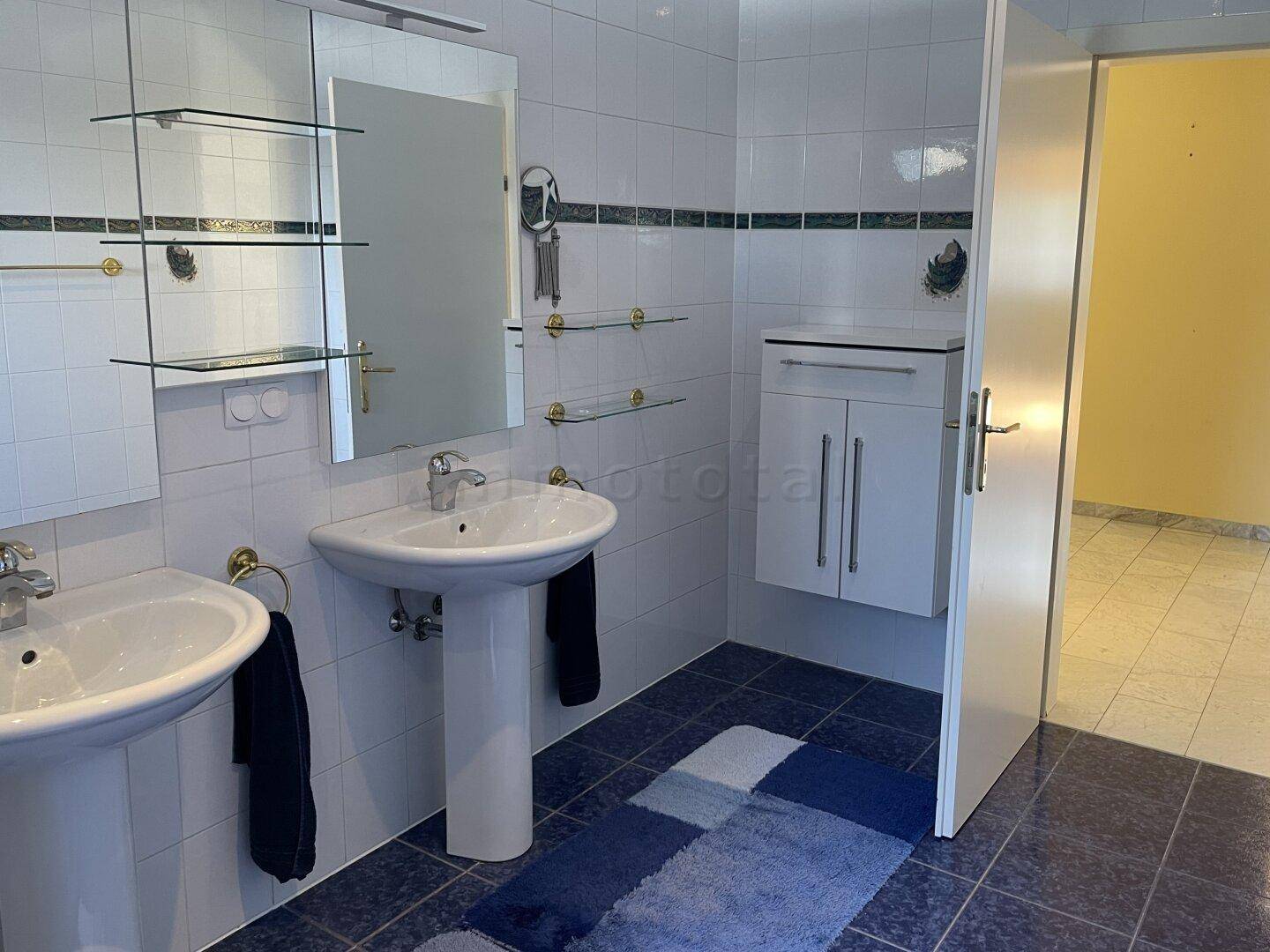 Helles Badezimmer im Dachgeschoss mit zwei Waschbecken, Spiegel und blauen Fliesen.